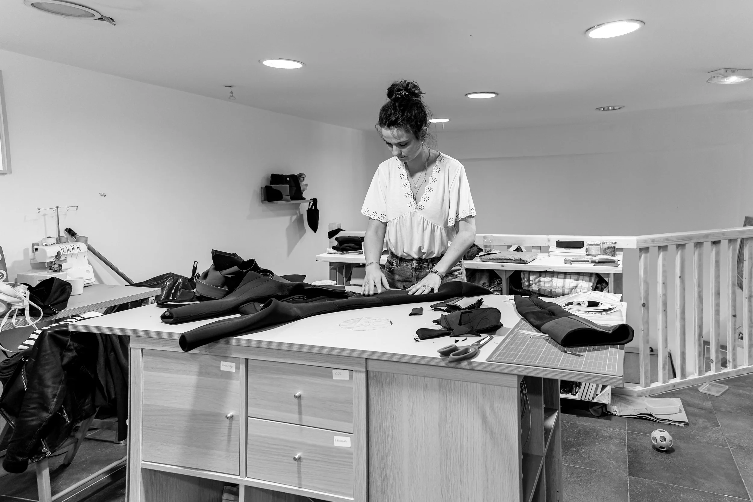 Une femme travaille sur du tissu ou du cuir dans un atelier ou un espace de couture, entourée d'outils de couture et de matériaux.