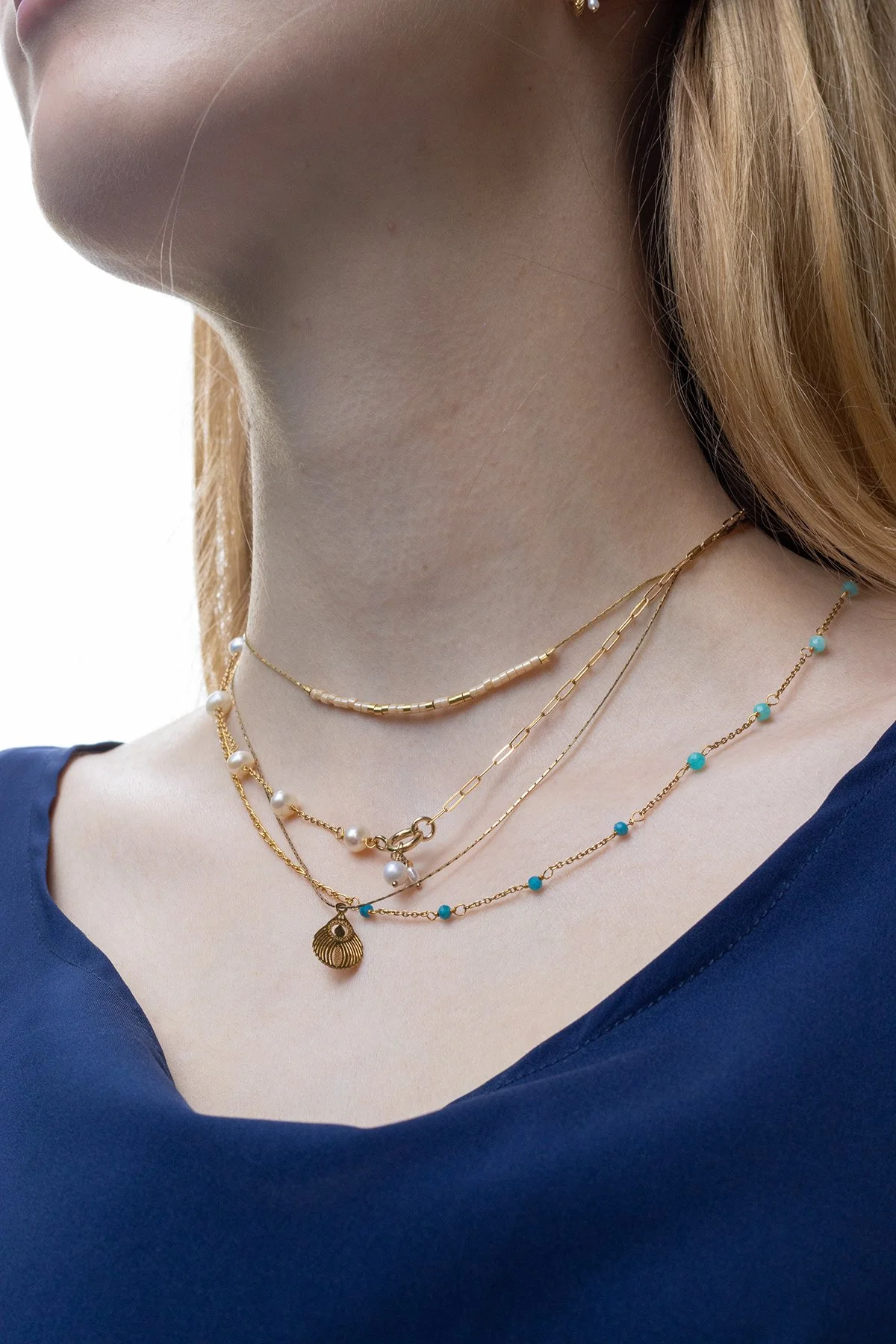 Close-up d'un cou de femme portant plusieurs colliers en or avec des perles blanches et turquoise.