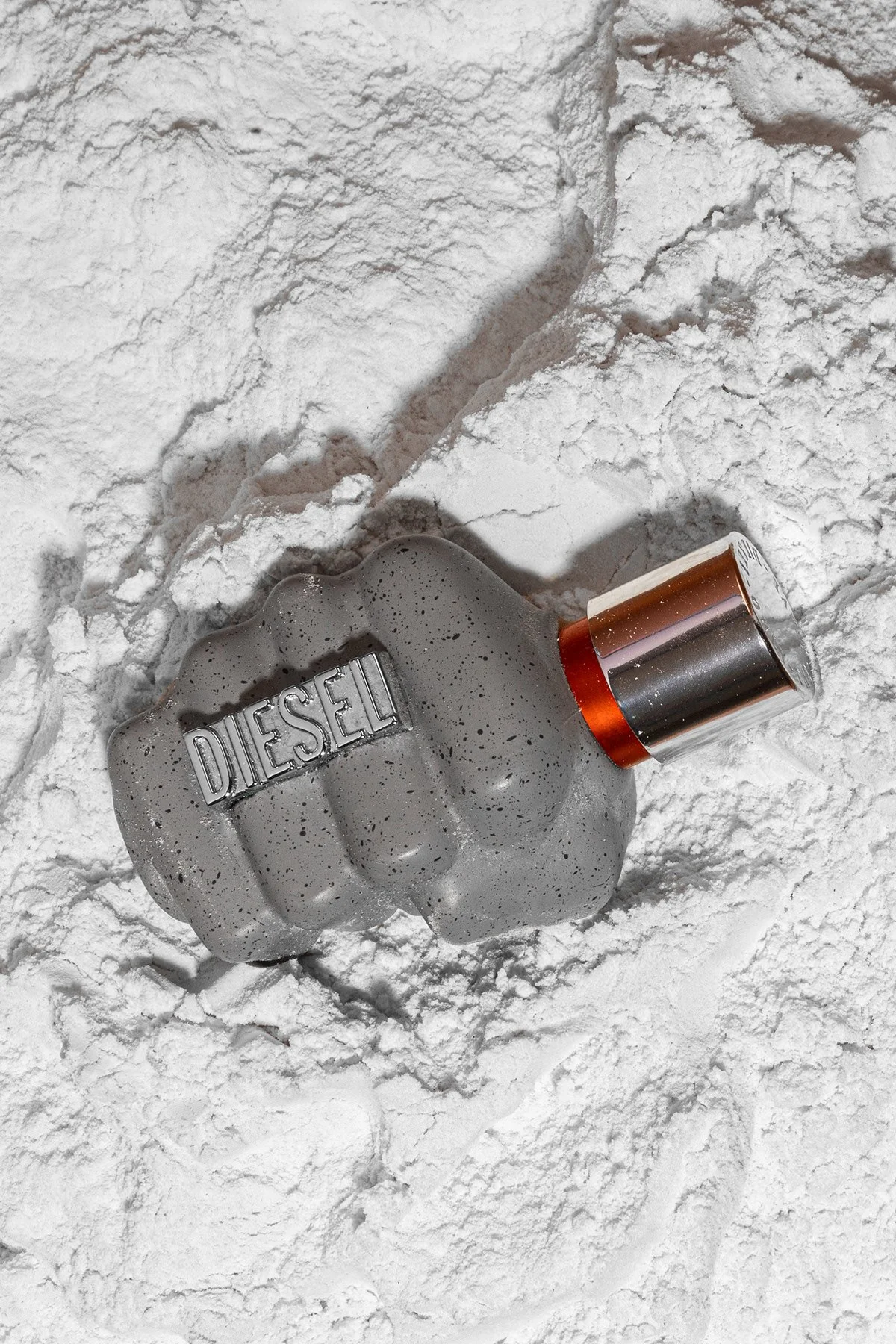 Flacon de parfum Diesel de couleur grise avec un bouchon métallique placé sur un sol blanc poudreux