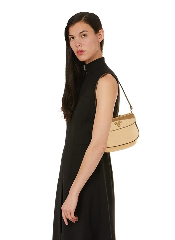 Une femme portant une robe noire sans manches et un sac à main beige avec un logo Prada.