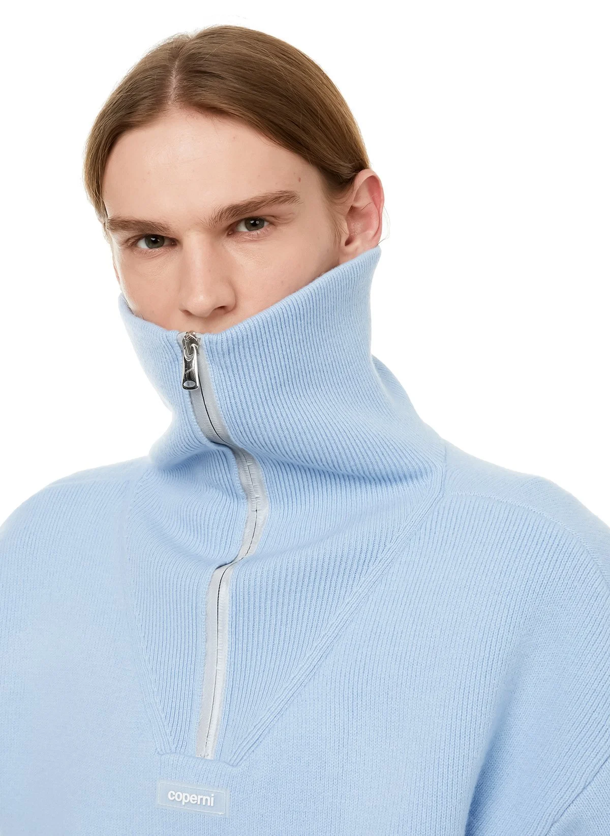 Jeune homme portant un pull d'hiver bleu clair avec un col montant zippé qui couvre une partie du visage.