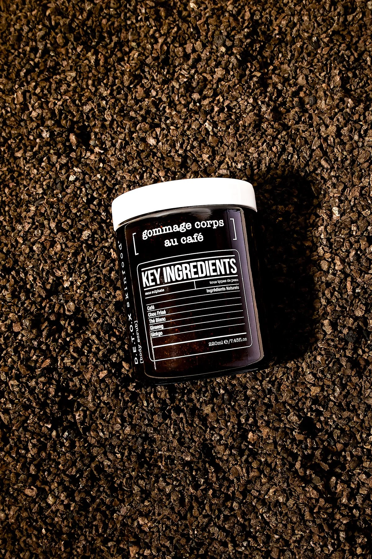 Pot de gommage pour le corps au café posé sur un lit de grains de café entiers.