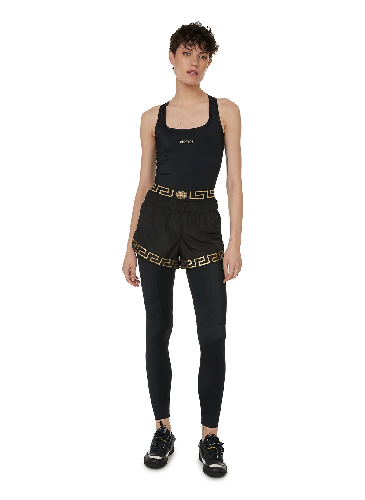 Une femme portant un ensemble de vêtements de sport noirs avec des détails dorés, y compris un bas et un haut, avec des chaussures de sport.