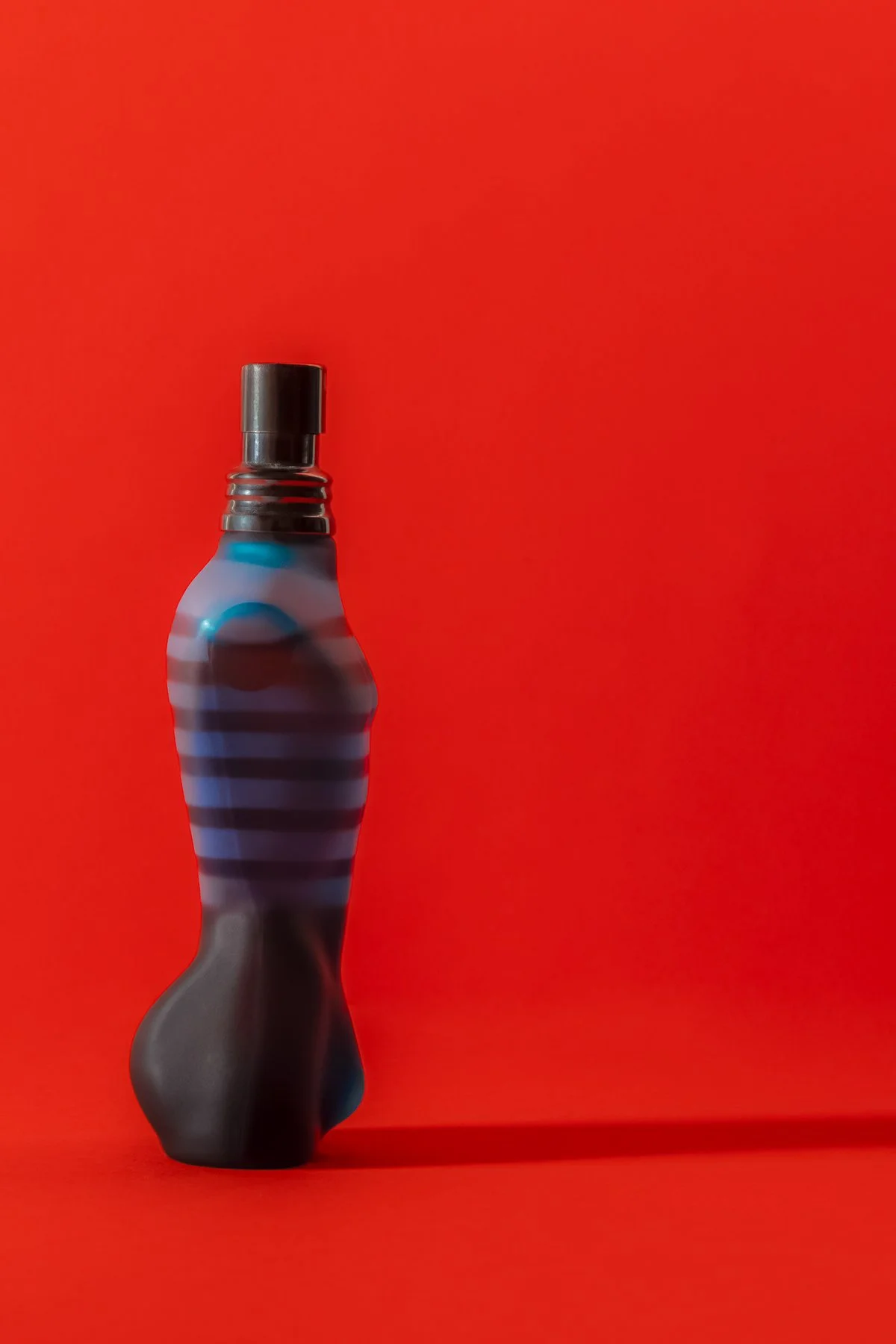 Une bouteille de parfum avec un design en forme de corps humain, rouge en arrière-plan.