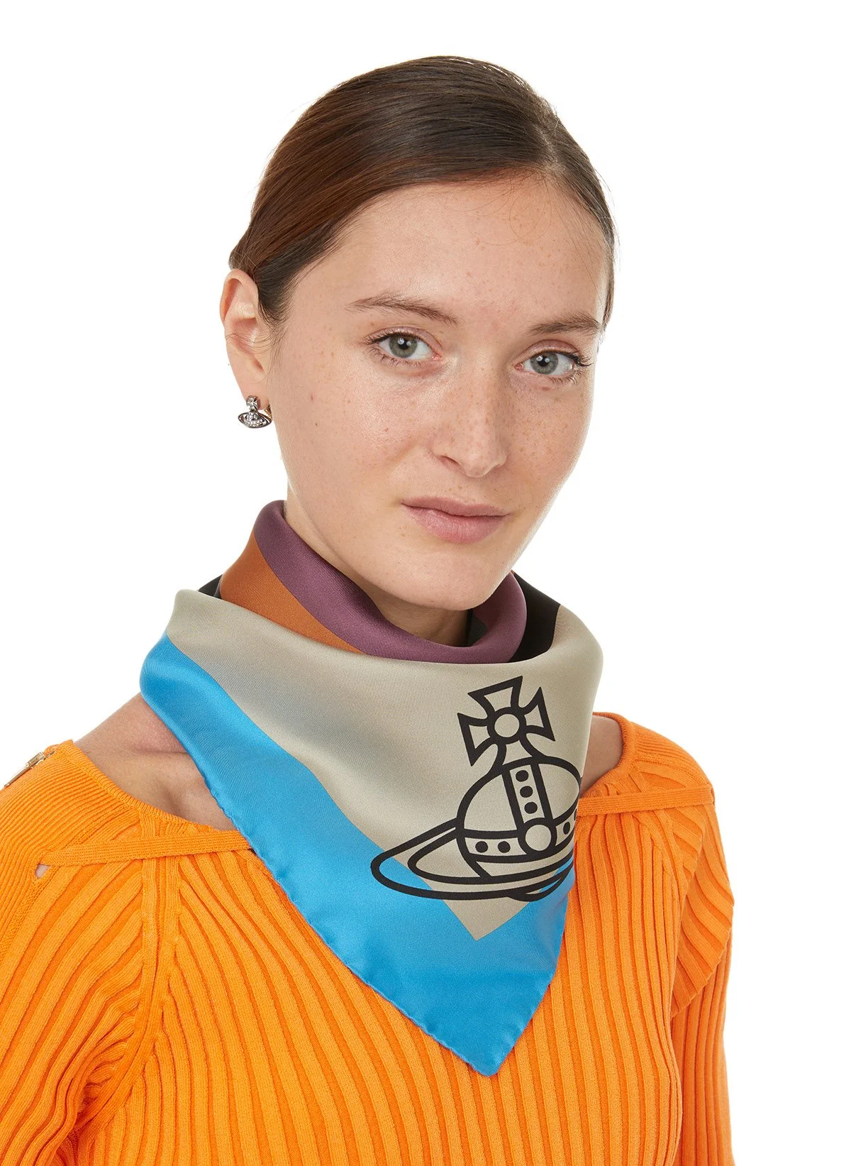 Jeune femme avec une écharpe colorée et un haut orange. Elle porte des boucles d'oreilles et a les cheveux bruns, coiffés en arrière. Background blanc.