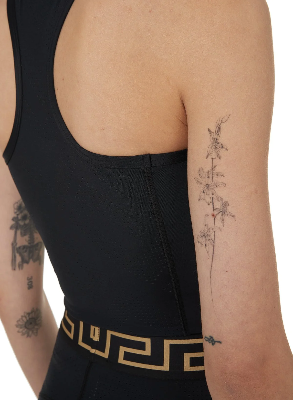 Bras noir et vêtements de sport noir avec détails en or, avec tatouages sur le bras gauche, dont un de fleurs et un de motif géométrique.