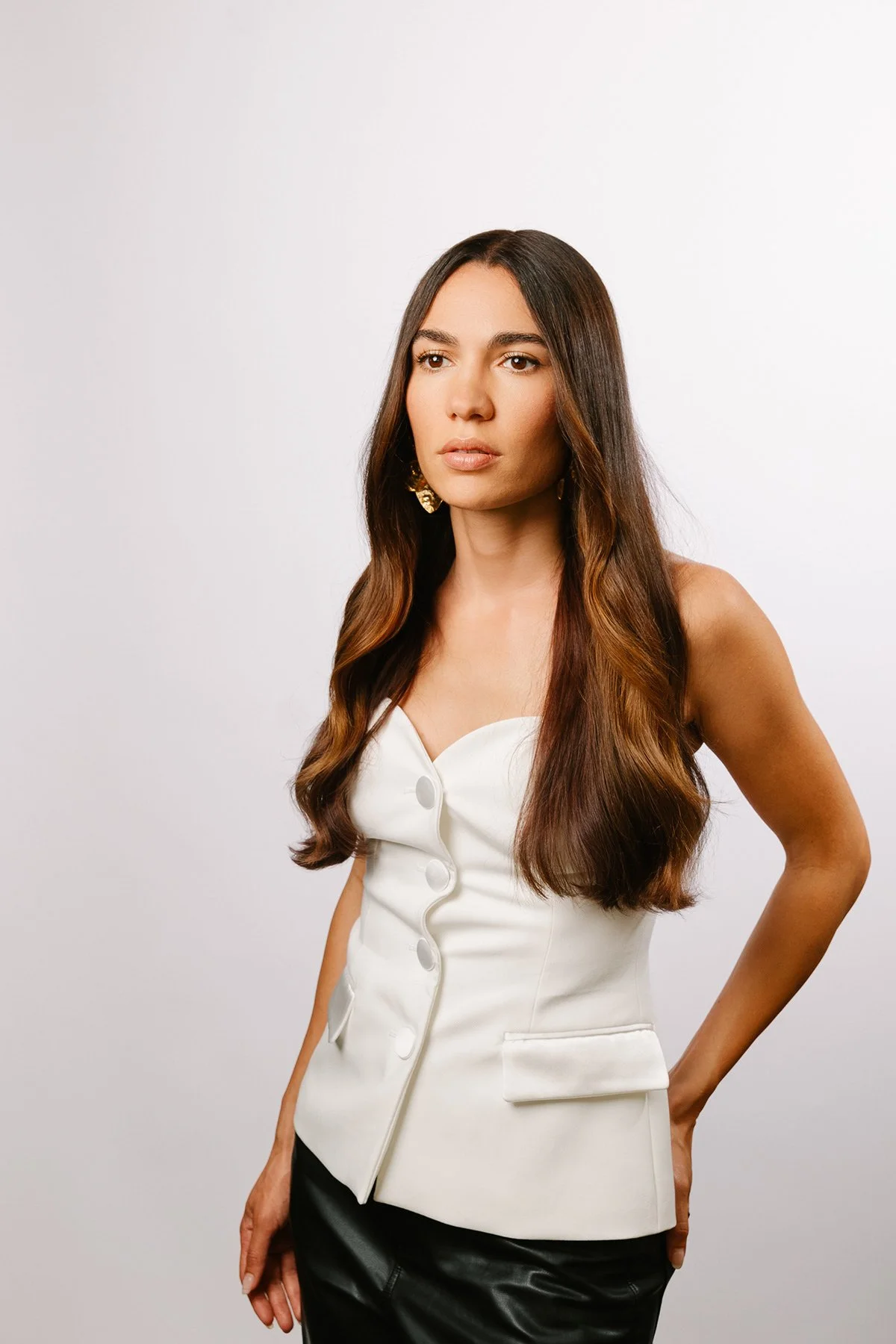 Femme avec cheveux longs, portant un haut blanc avec boutons, sur fond blanc.