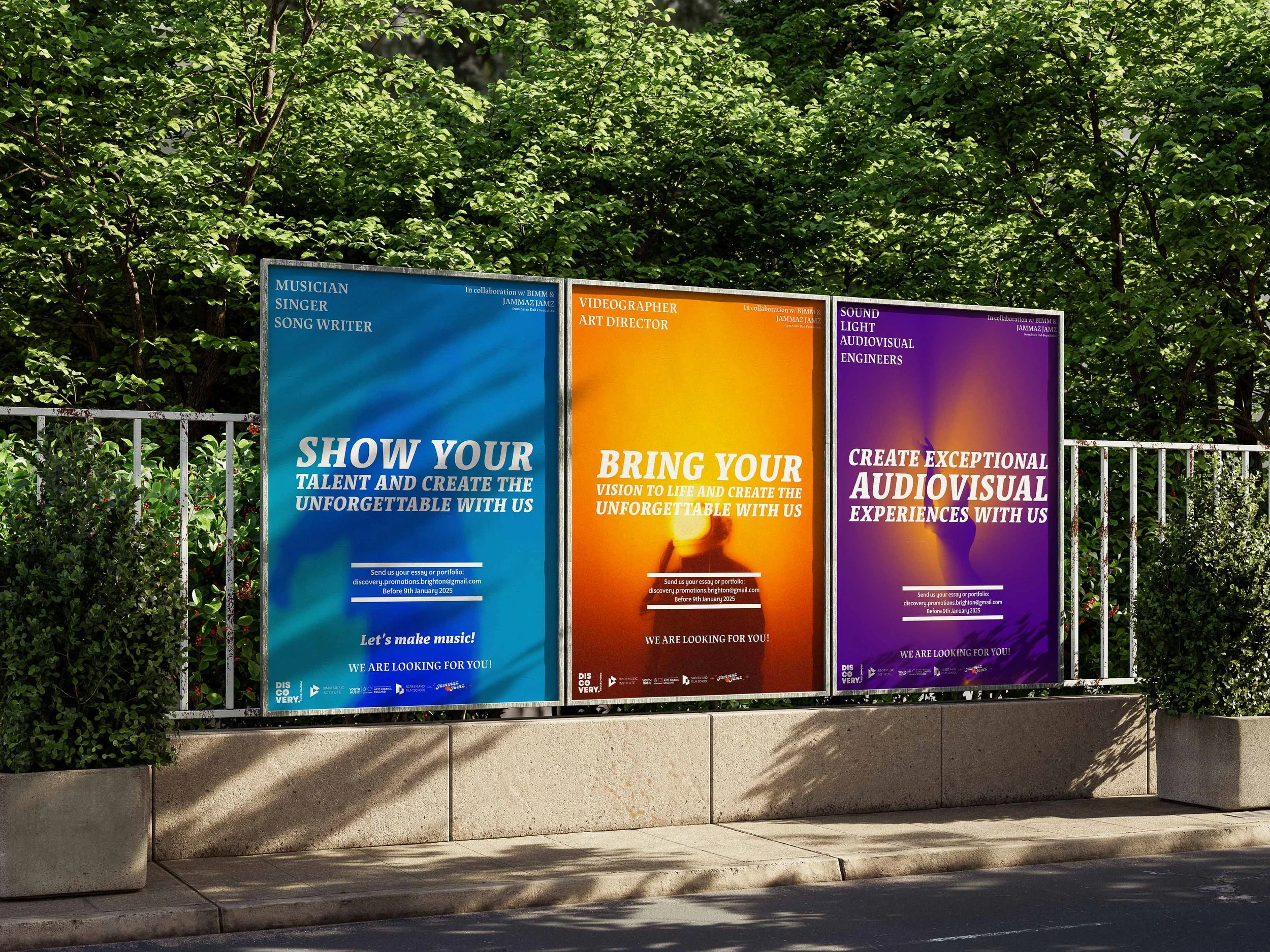 Trois affiches publicitaires colorées en bleu, orange et violet sur une barrière en métal, entourées de verdure, avec du texte promotionnel en anglais pour des événements musicaux et audiovisuels.