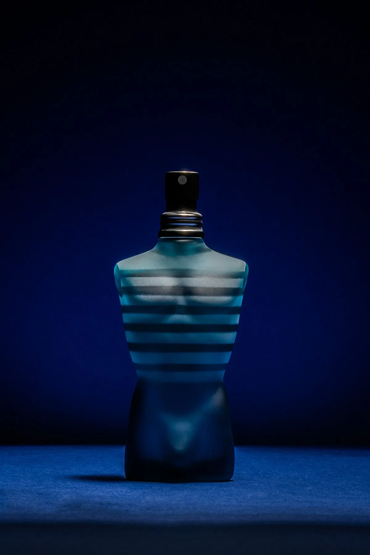 Bouteille de parfum bleue avec rayures noires, sur fond sombre et éclairage mettant en valeur sa forme