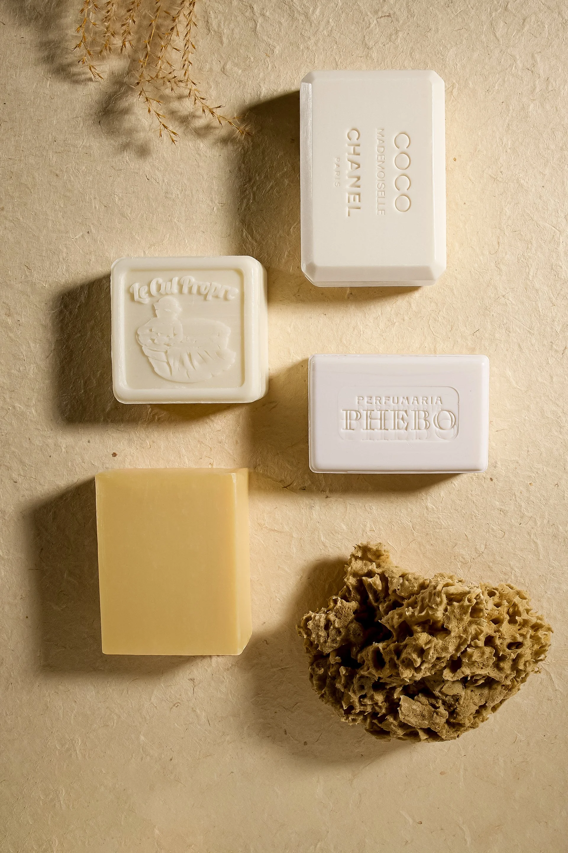 Différents savons et un éponges naturel sur une surface beige.