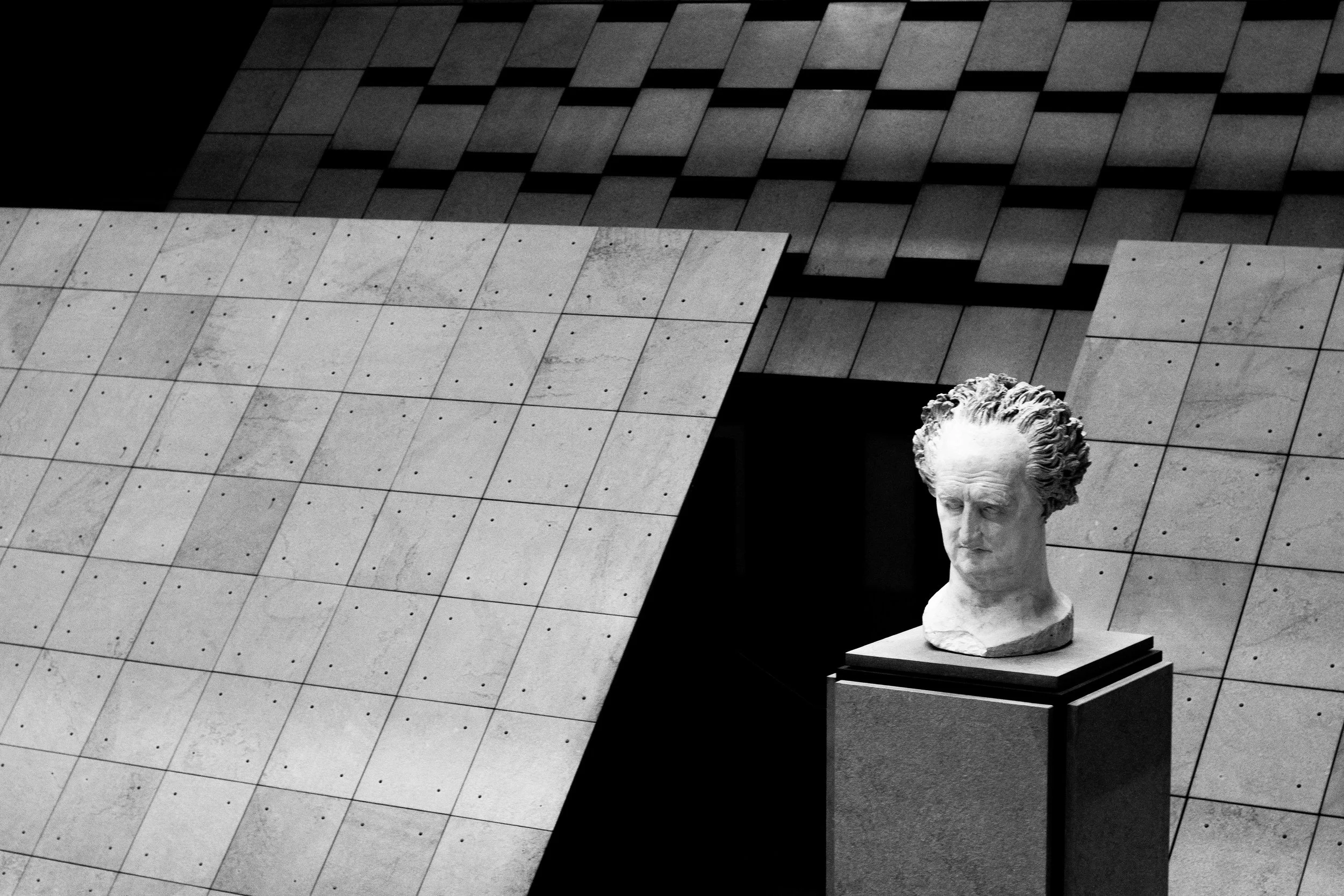 Statue en marbre d'une tête humaine sur un socle dans un espace moderne avec des murs en béton.