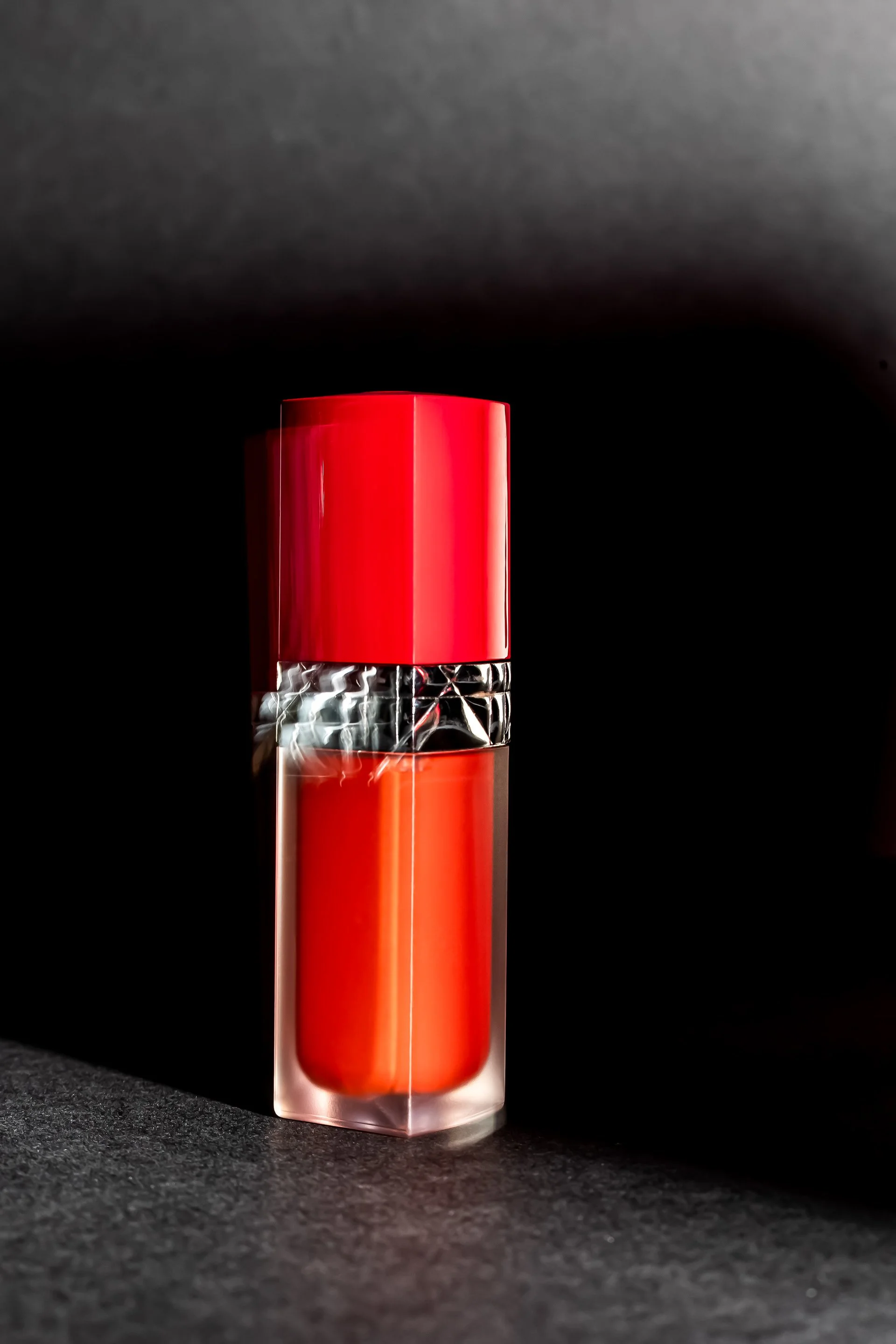 Rouge à lèvres dans un tube transparent avec un capuchon rouge, placé sur une surface noire avec un fond noir.