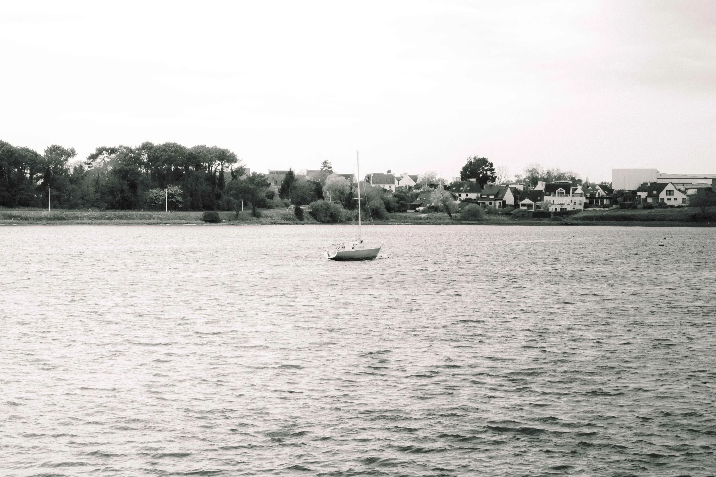 Un bateau à voile au centre d'un lac avec un village résidentiel en arrière-plan.