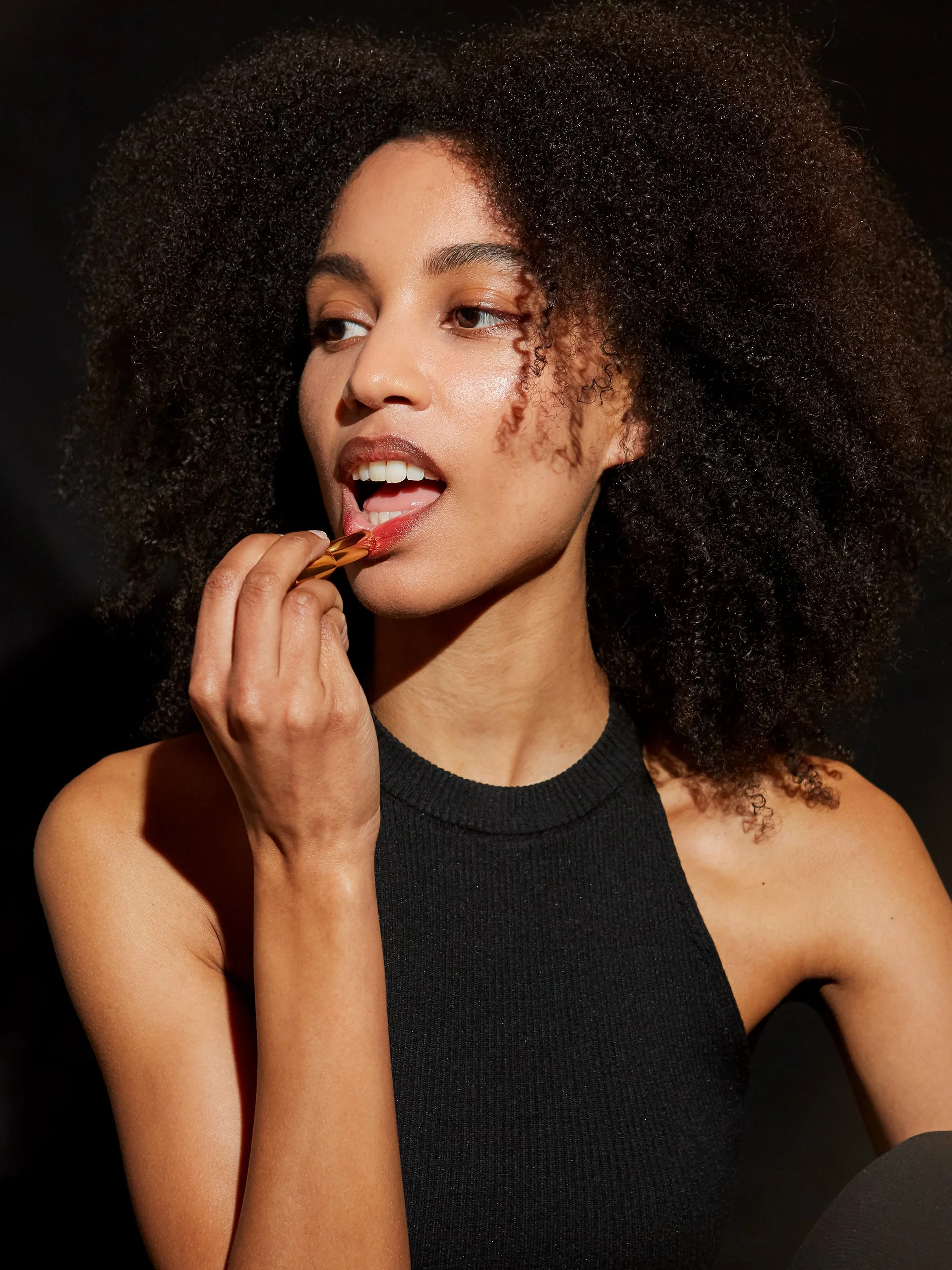 Jeune femme noire avec de grosses boucles d'oreilles, mangeant un bonbon.