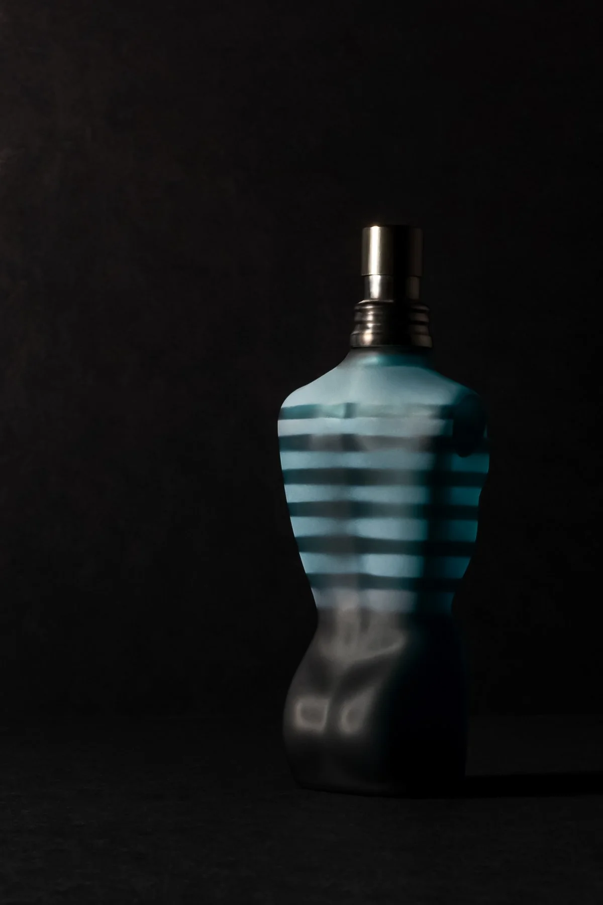 Flacon de parfum au design incliné, avec des rayures bleues et argentées, contre fond noir.