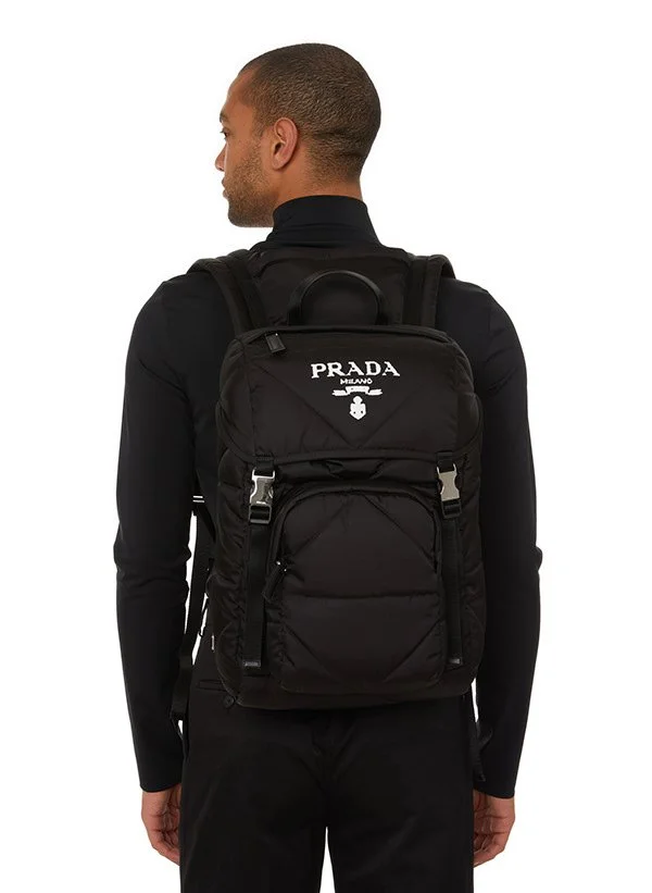 Homme vu de dos portant un sac à dos noir Prada Milano contre un fond blanc.