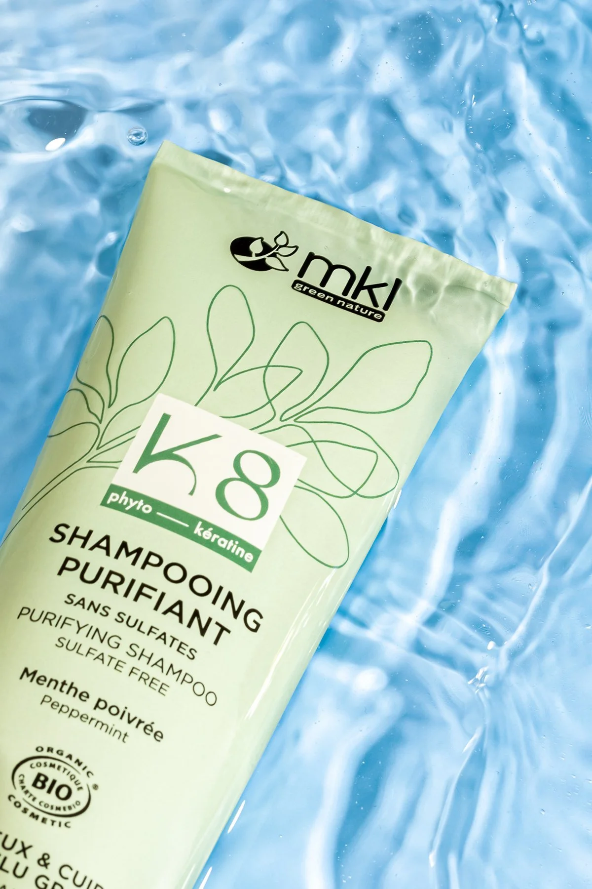 Bouteille de shampooing purifiant à la menthe poivrée de la marque mkl, posé sur une surface d'eau bleue.