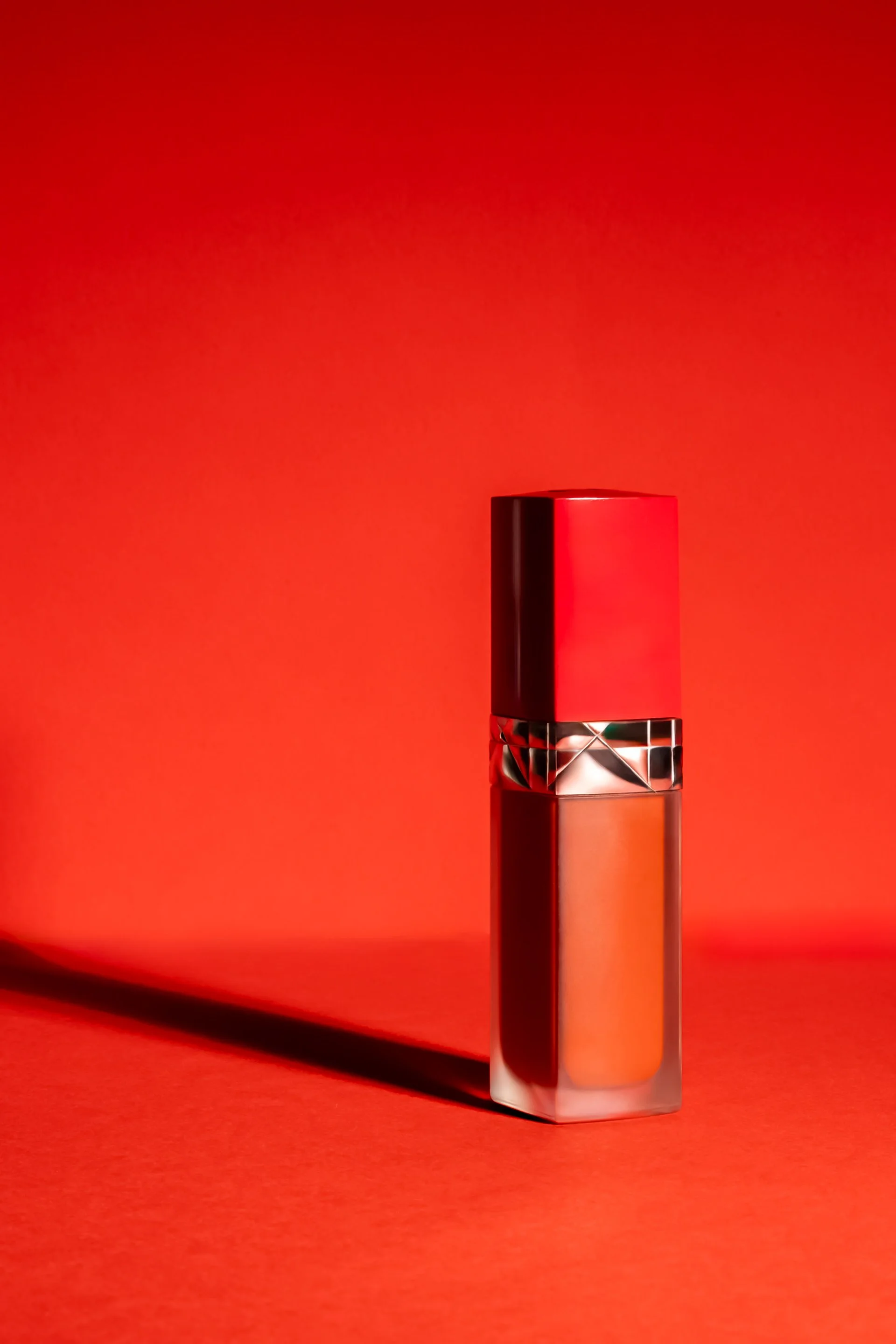 Un flacon de vernis à ongles rouge sur un fond rouge, avec une ombre portée vers la gauche.