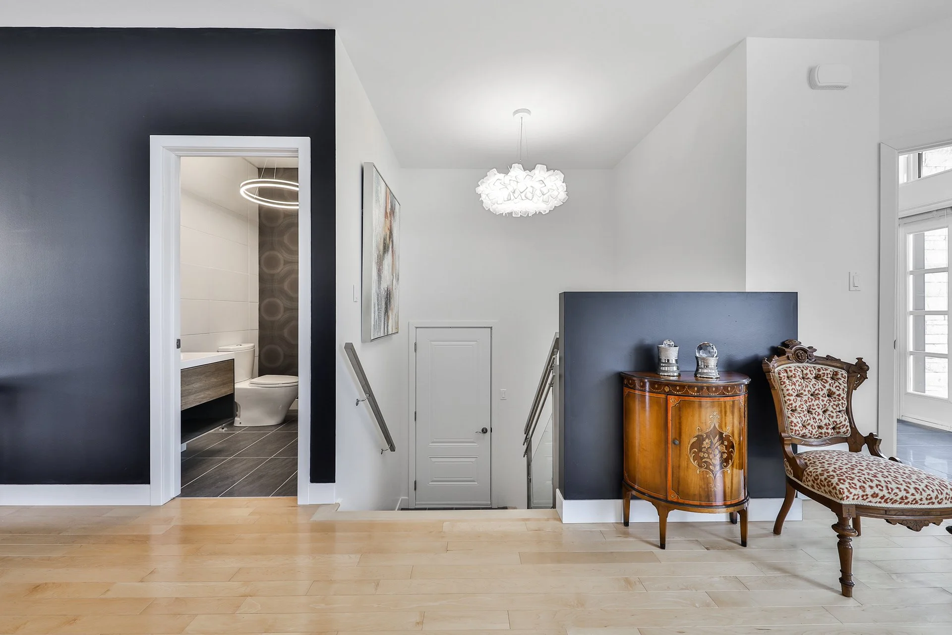 Intérieur d'une maison avec escalier, mobilier ancien, peinture moderne, et salle de bain visible à gauche.
