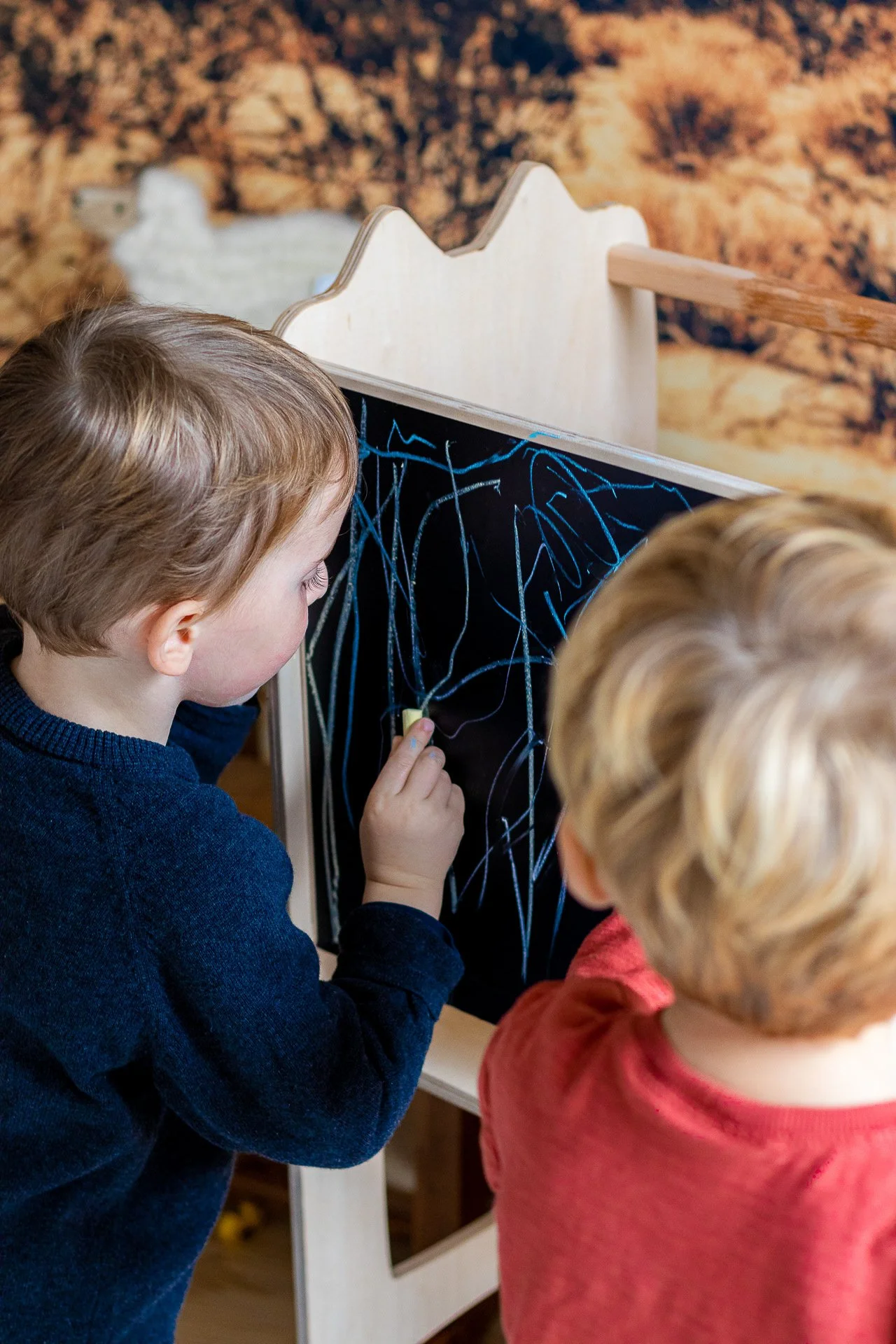 Deux enfants jouent avec une ardoise noire et des craies, dessinant avec des lignes blanches et bleues.