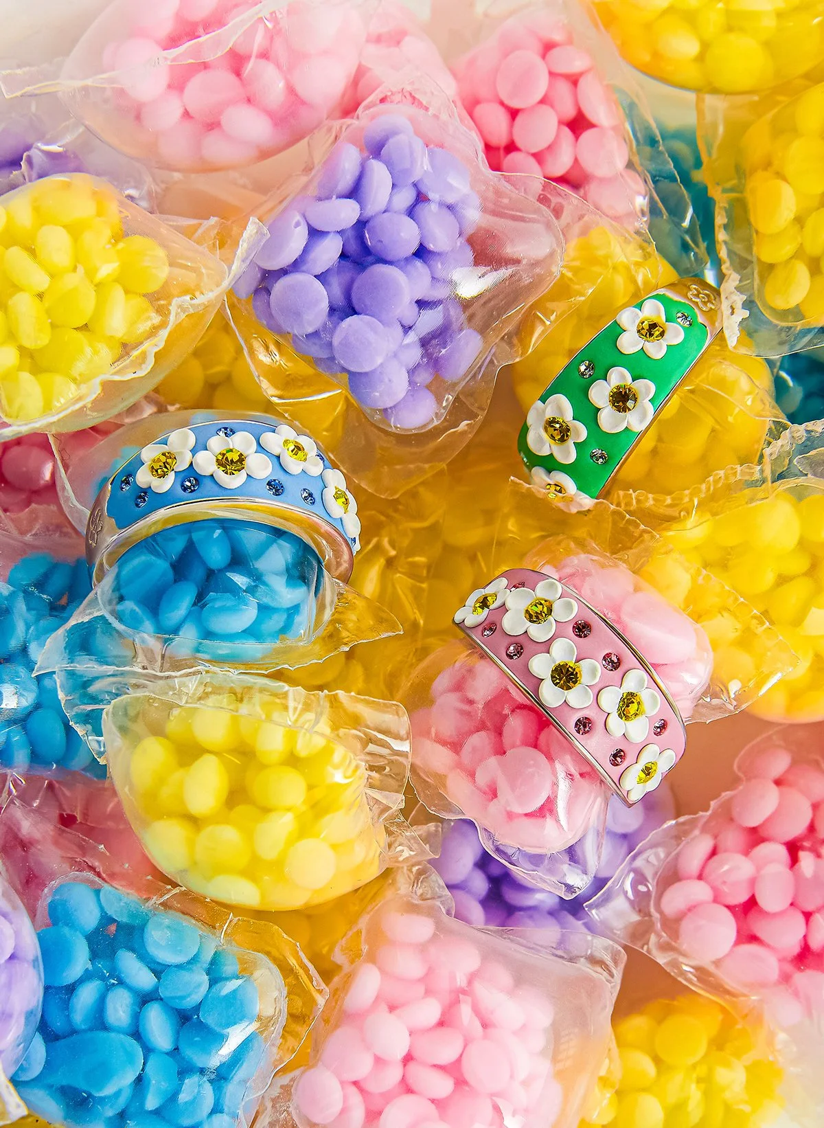 Bonbons colorés en sac en plastique, comprenant des bonbons roses, jaunes, bleus, violets et blanc avec des décorations florales et des brillants.
