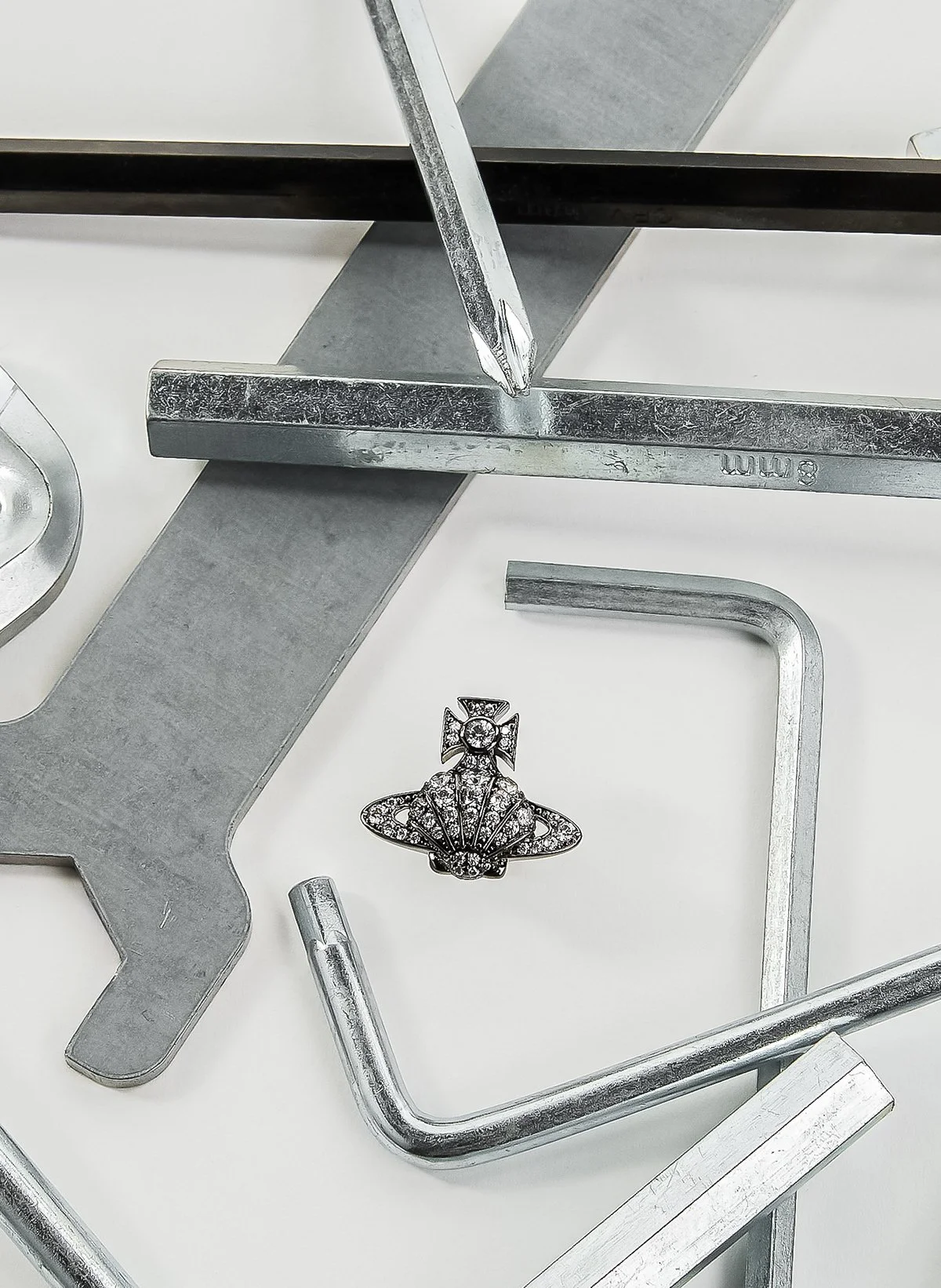 Un bijou en forme d'ange décoré de pierres précieuses, entouré de divers outils métalliques de bijoux, posés sur une surface blanche.