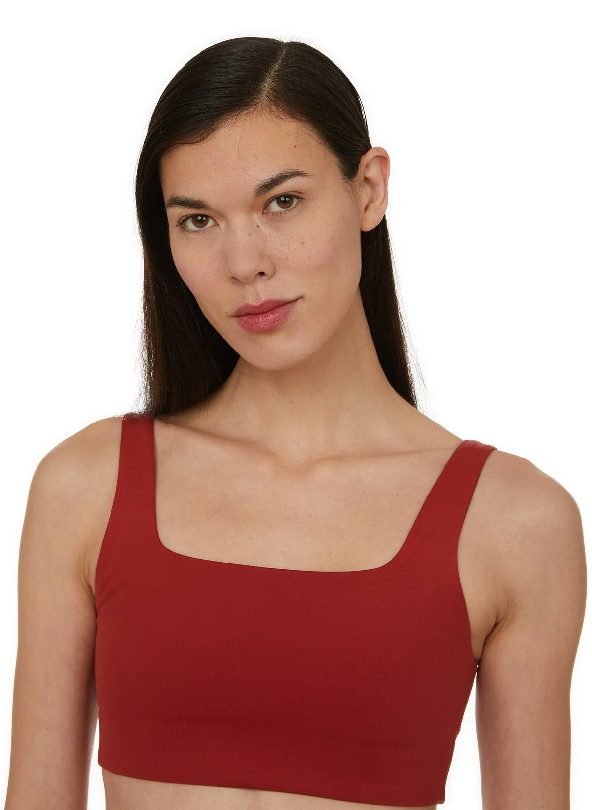 Jeune femme avec des cheveux longs, portant un haut rouge à bretelles, regardant la caméra avec une expression neutre, fond blanc.