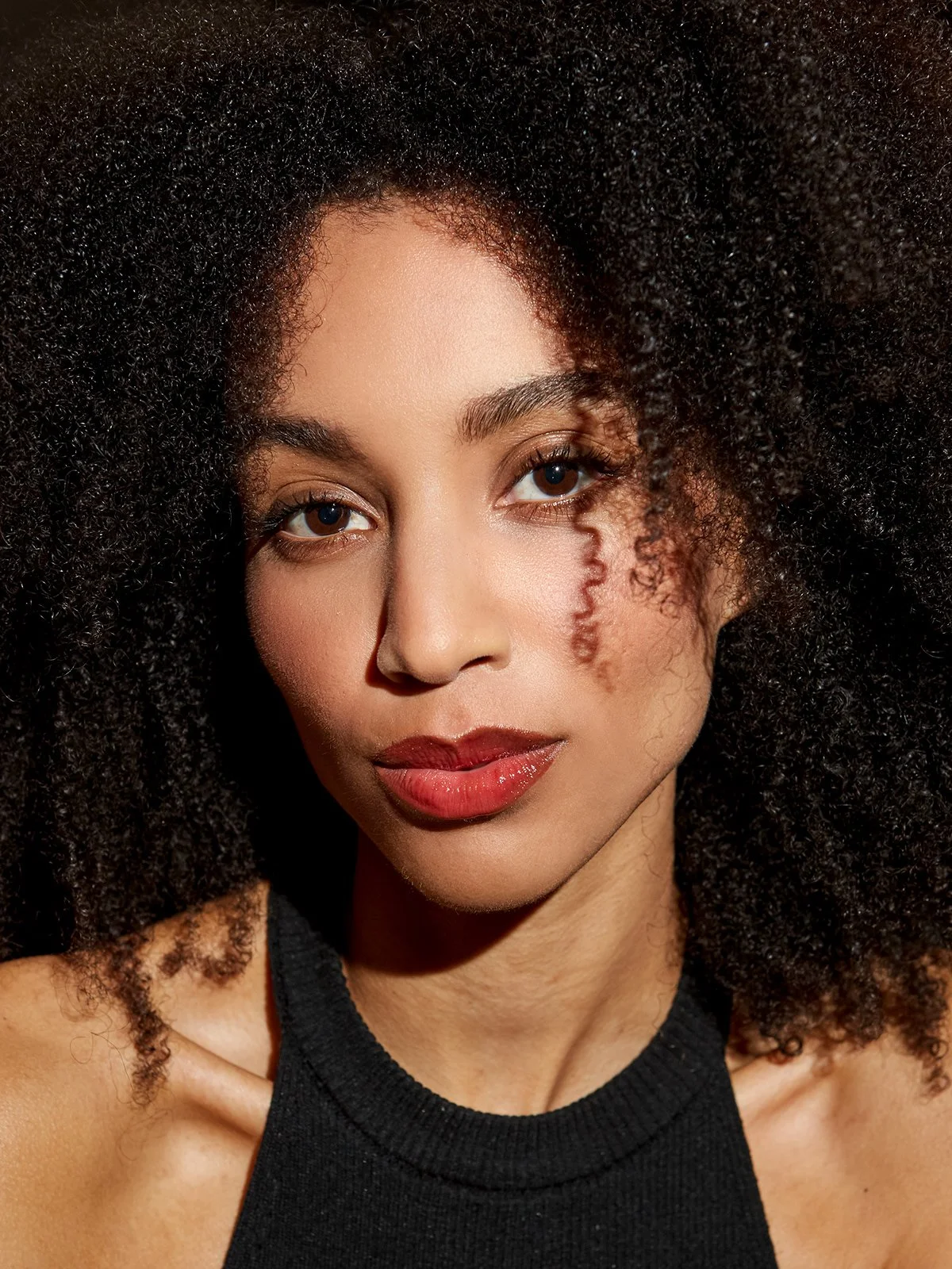 Un portrait en gros plan d'une femme avec des cheveux bouclés et un maquillage naturel. Elle porte un haut noir.