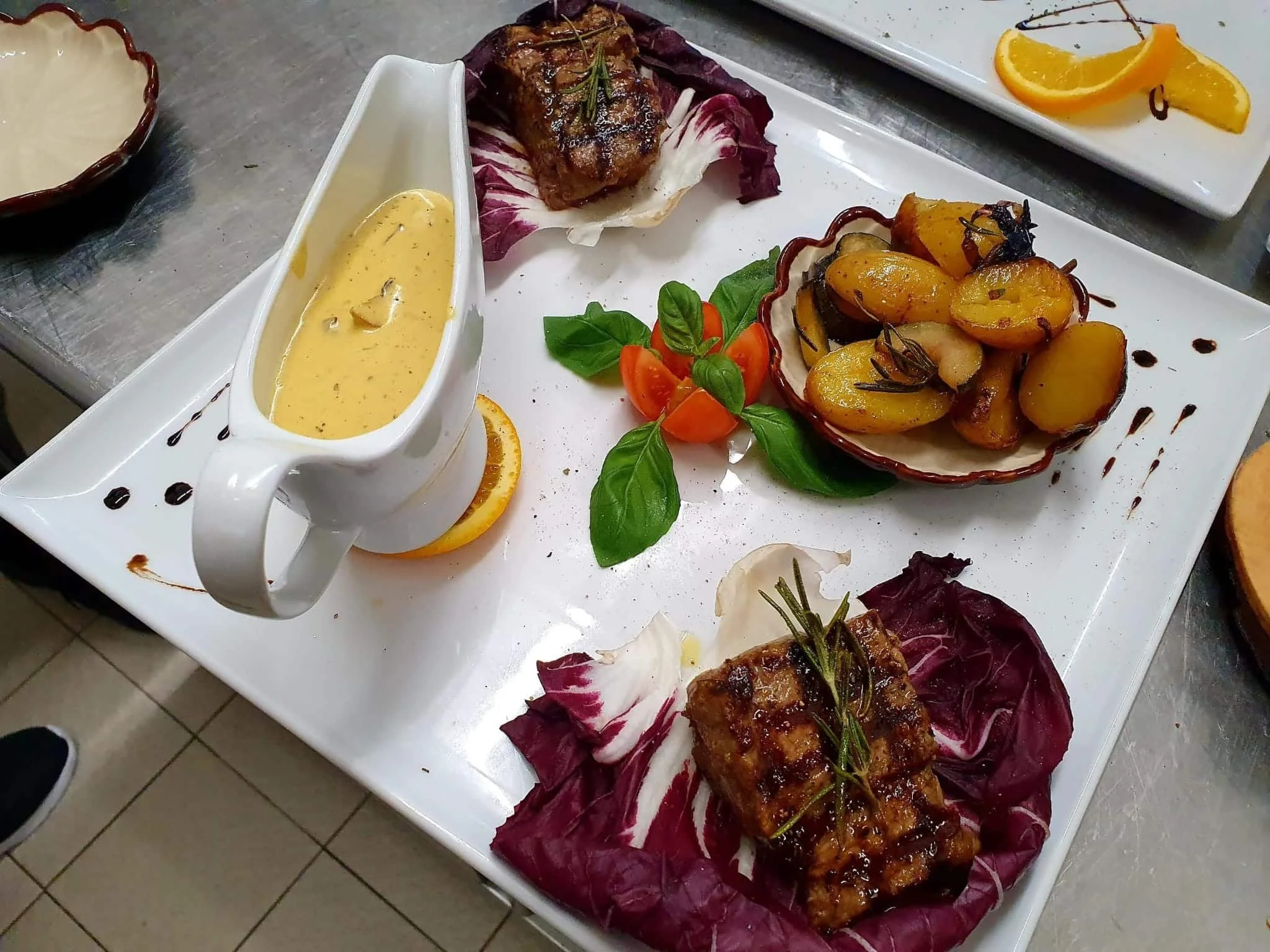 Ein Teller mit mehreren Gerichten, darunter Braten, Kartoffeln, Gemüse, Sauce und Garnituren, auf einer weißen Platte.