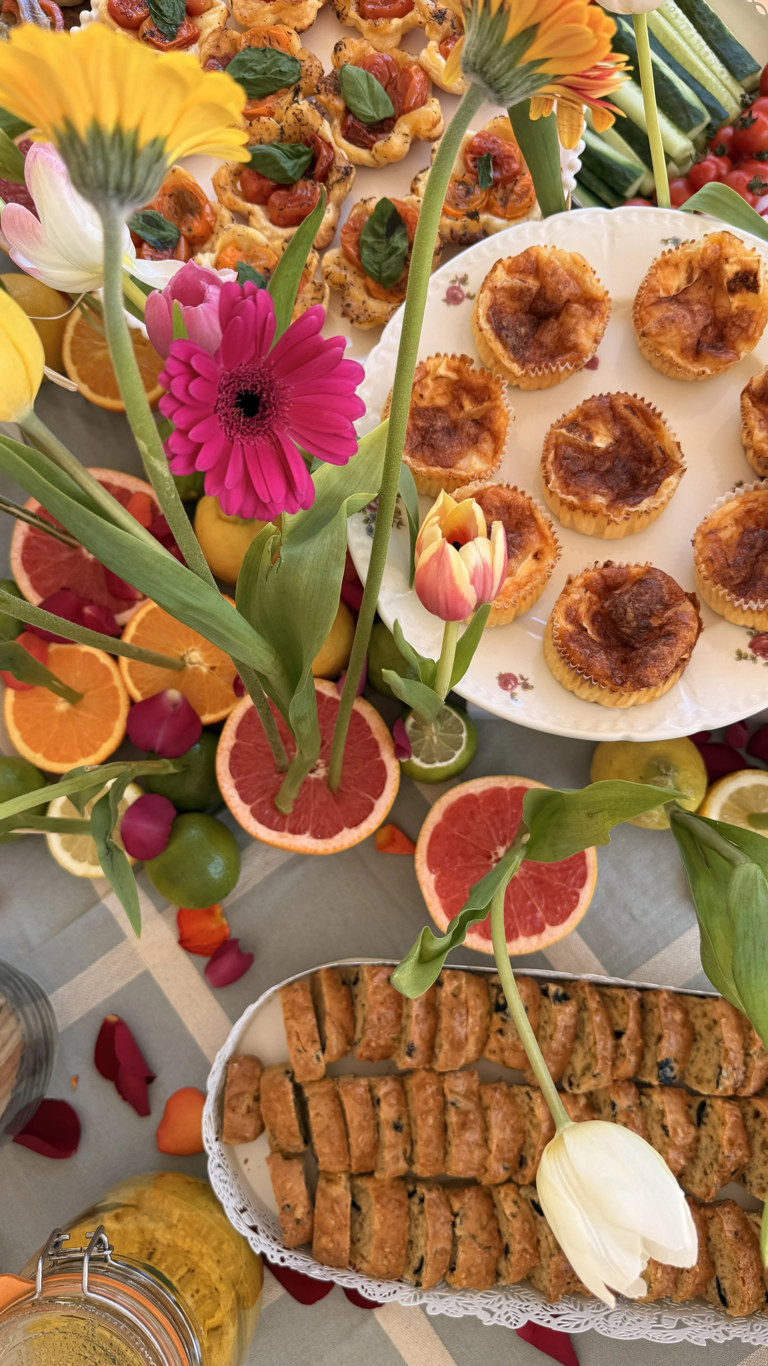 A table filled with colorful flowers and an assortment of food items, including pastries, citrus slices, and fruit garnishes.