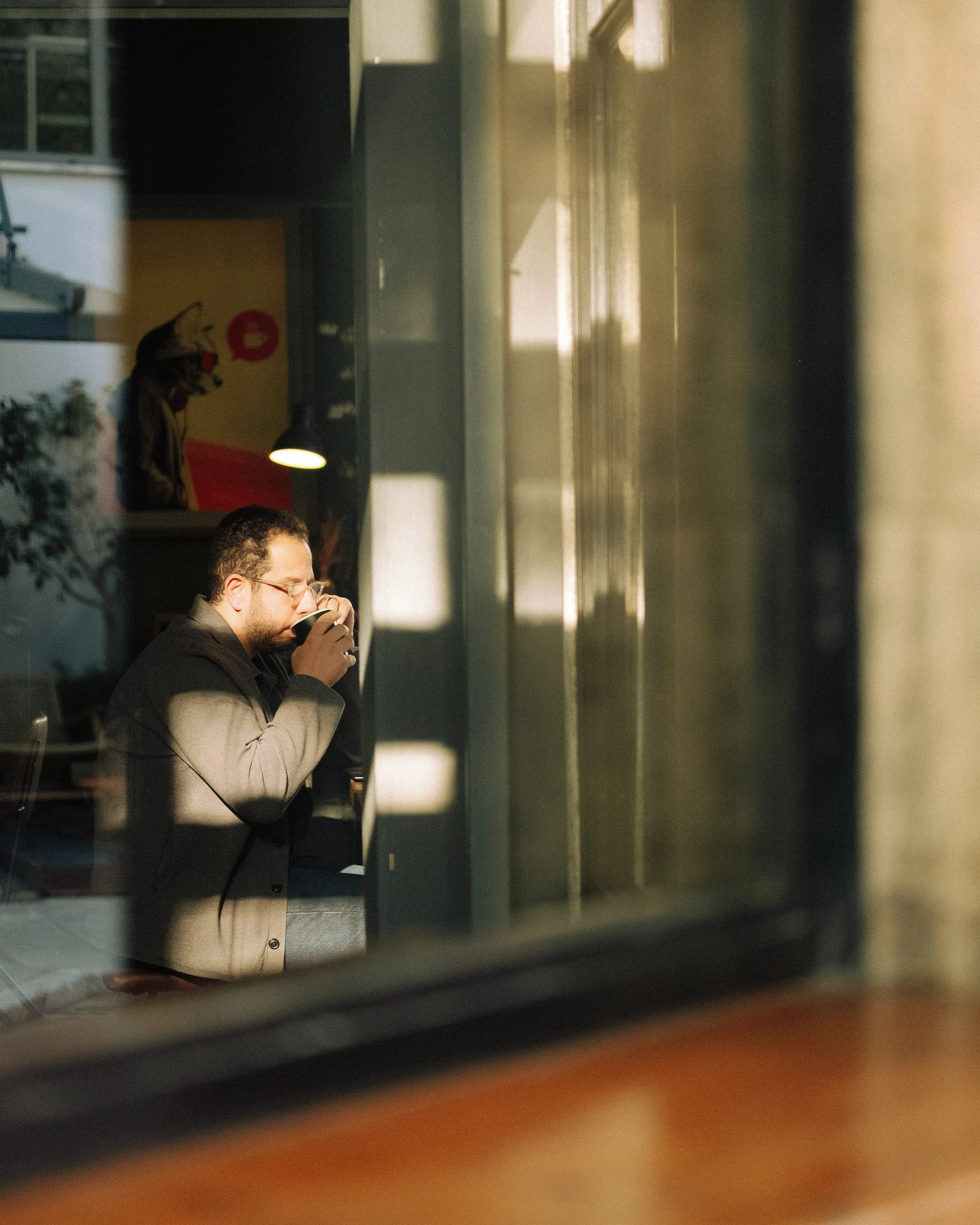A man sitting in a room with sunlight coming through a window, holding a phone, with a dog statue or figure in the background.