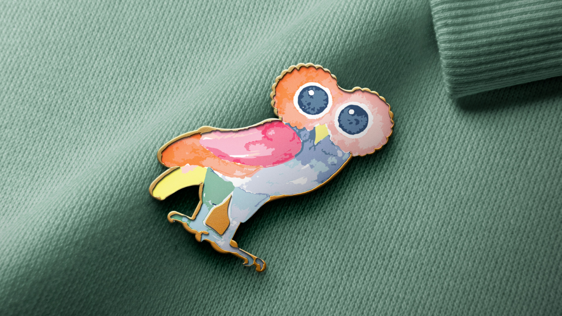 Colorful owl-shaped enamel pin with large eyes, perched on a green fabric background.