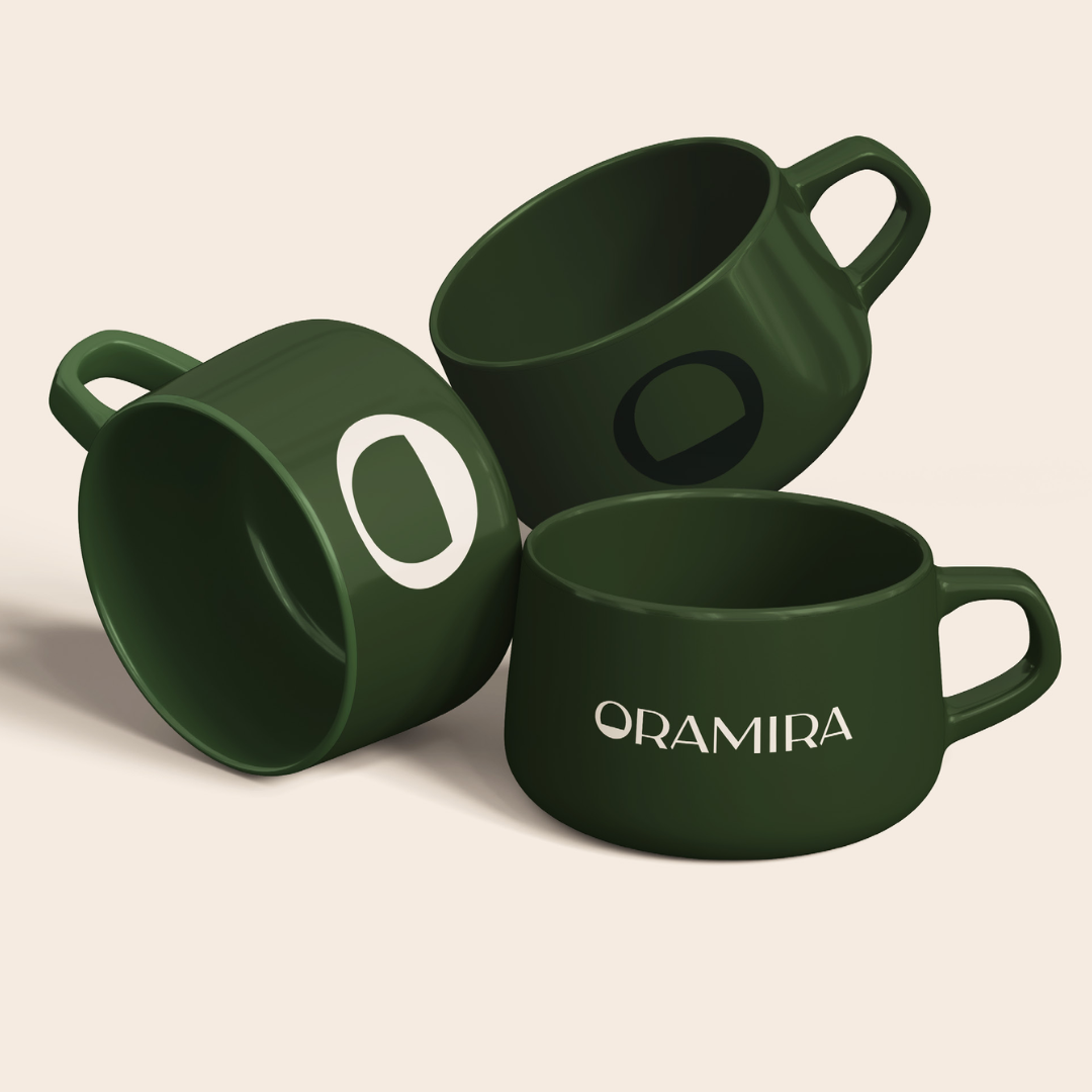 Three dark green ceramic coffee mugs, one with the word 'ORAMIRA' printed on it, arranged on a plain light background.