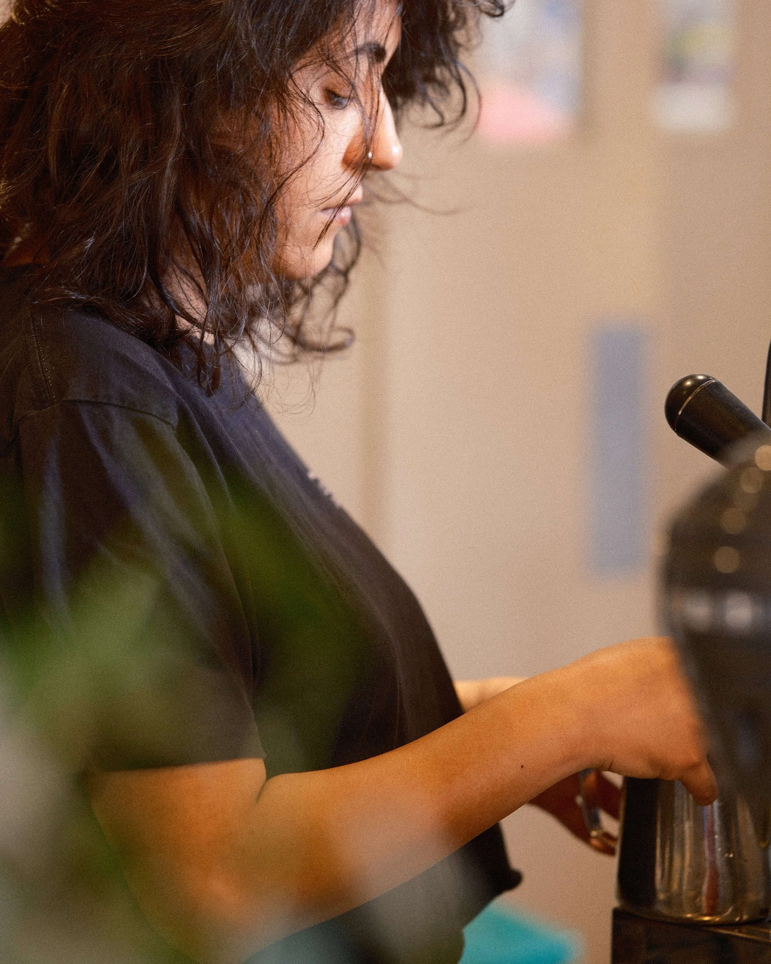 A woman with curly hair and a nose ring looking down, using a microscope.