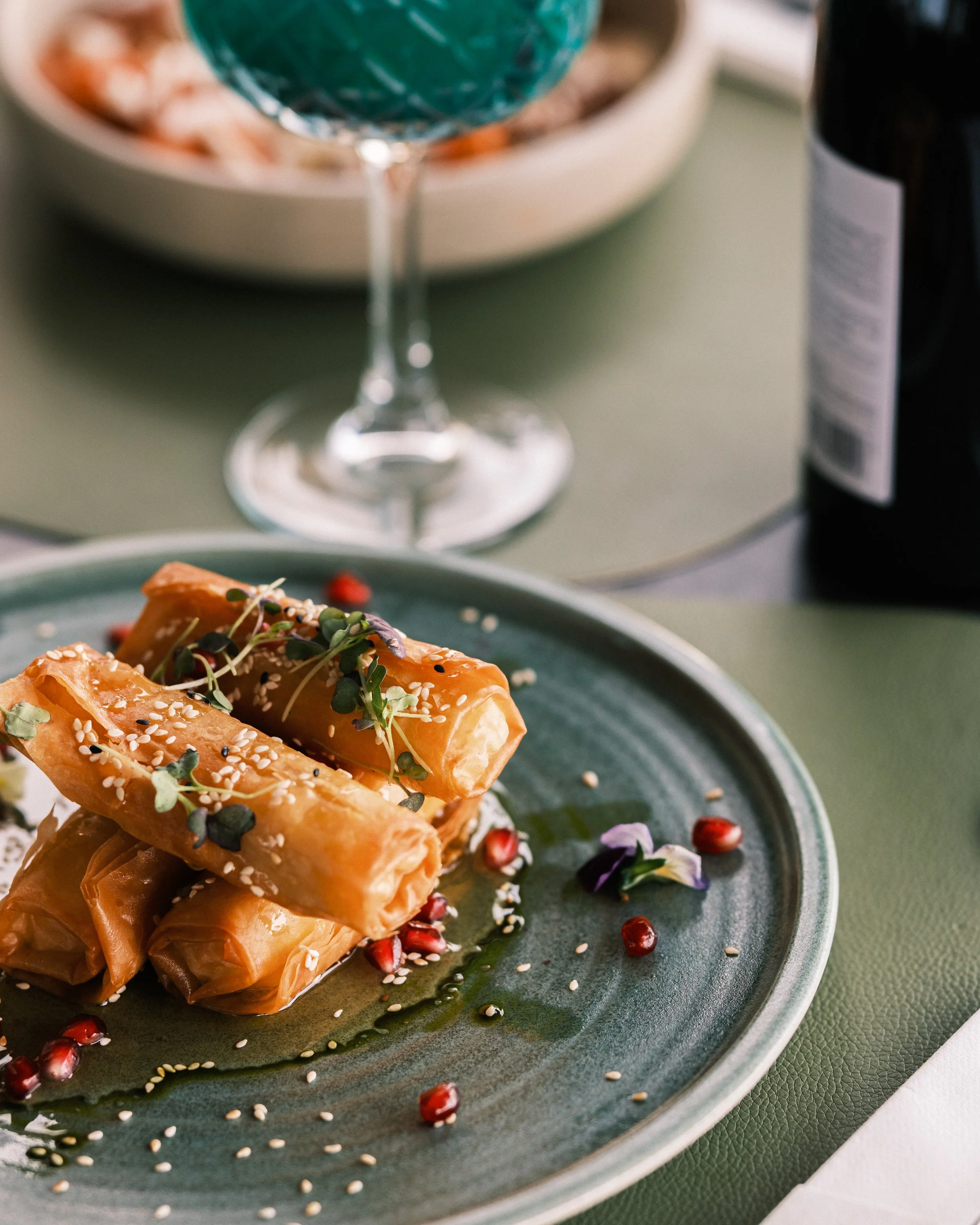 Plate of Asian-inspired roasted salmon garnished with microgreens, sesame seeds, and pomegranate seeds, served with sauce and surrounded by decorative edible flowers.