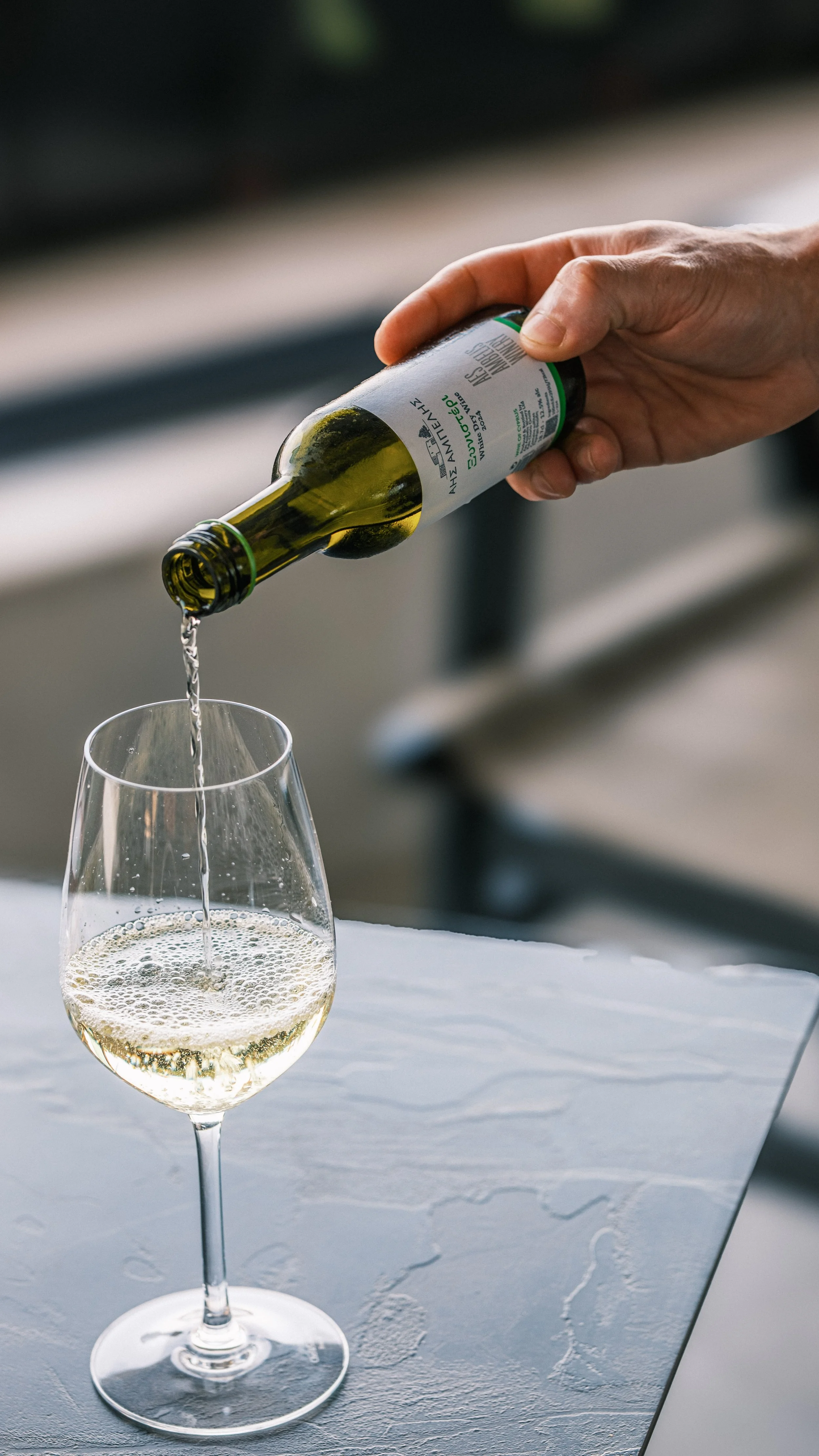 Hand pouring white wine into a glass on a table.