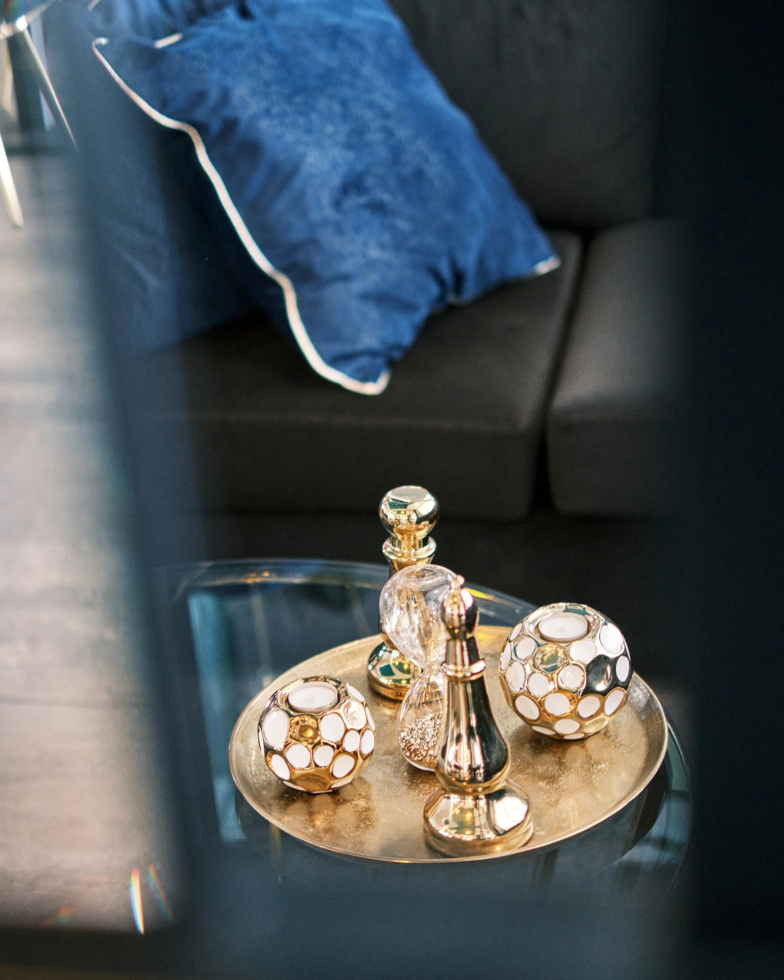 Decorative candle holders on a round tray, holding candles, with a black sofa and a blue pillow in the background.