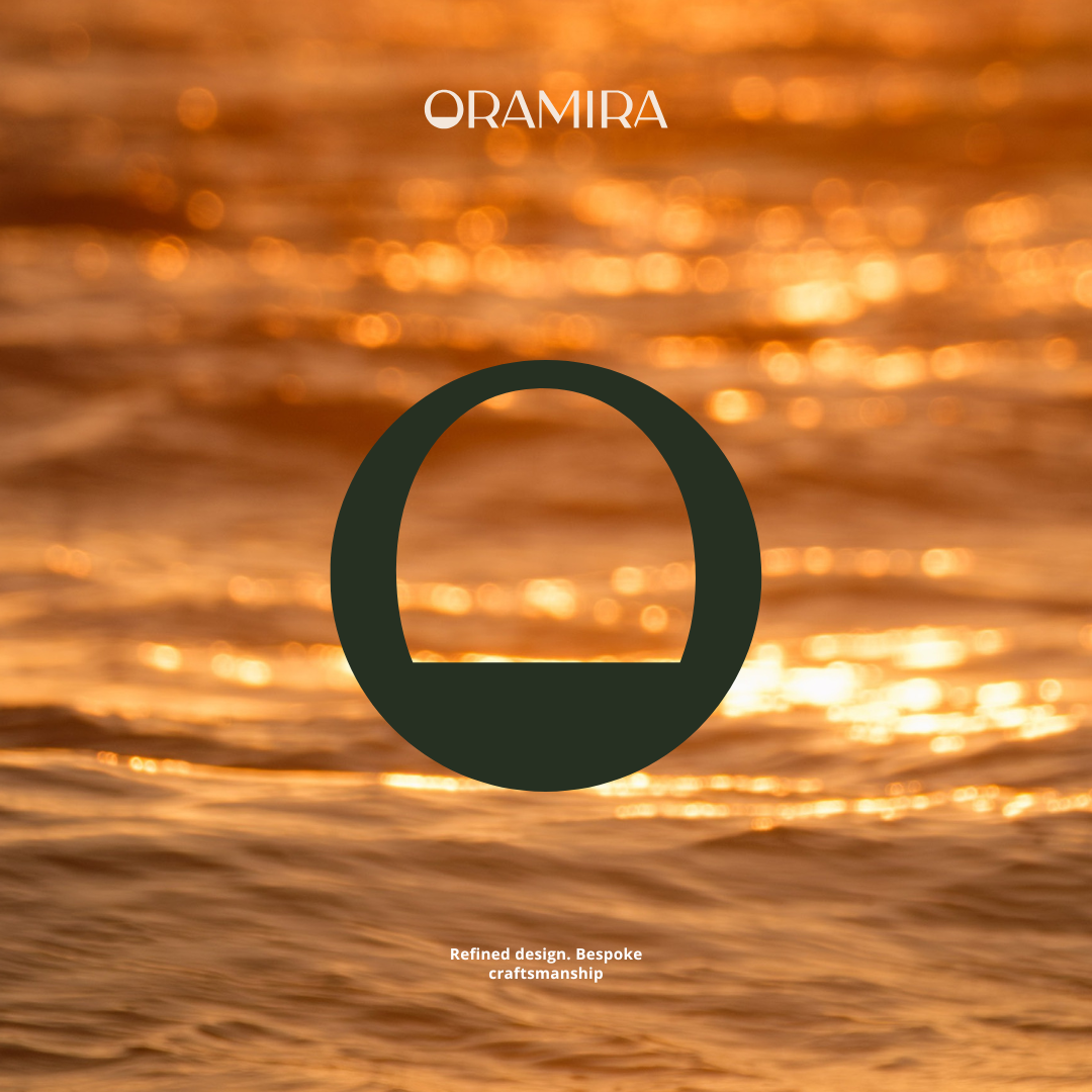 A blurred golden ocean scene at sunset with a large dark circular emblem in the center. The text 'ORAMIRA' appears at the top, and 'Refined design. Bespoke craftsmanship' is written at the bottom.
