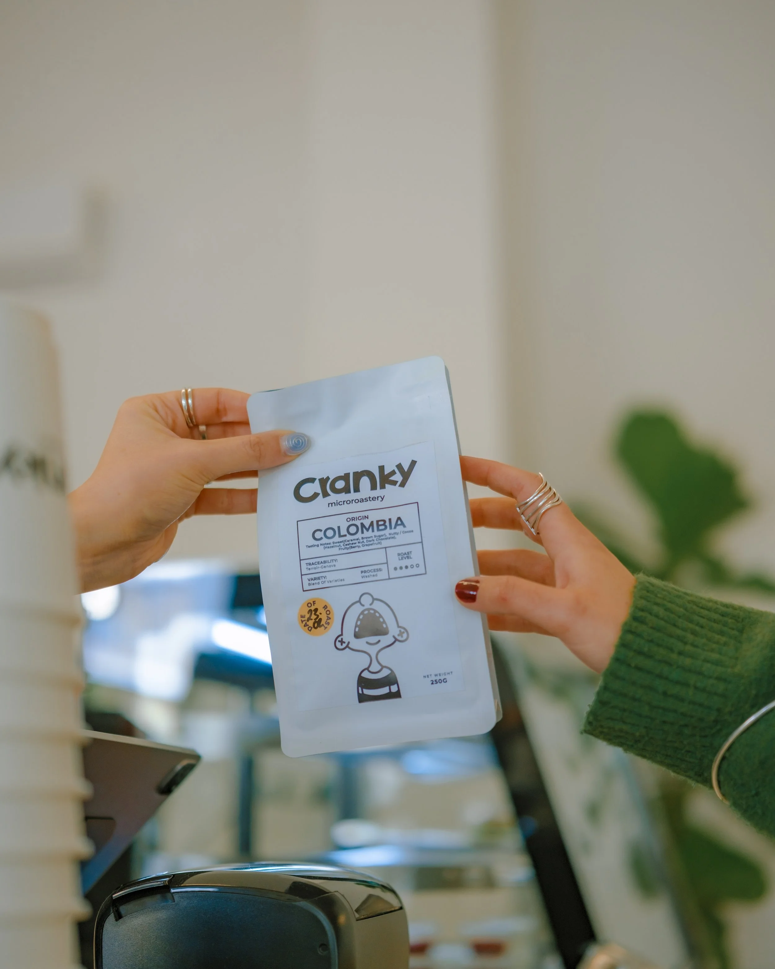 Person holding a bag of Cranky micro-roastery coffee, with a blurred background of indoor setting