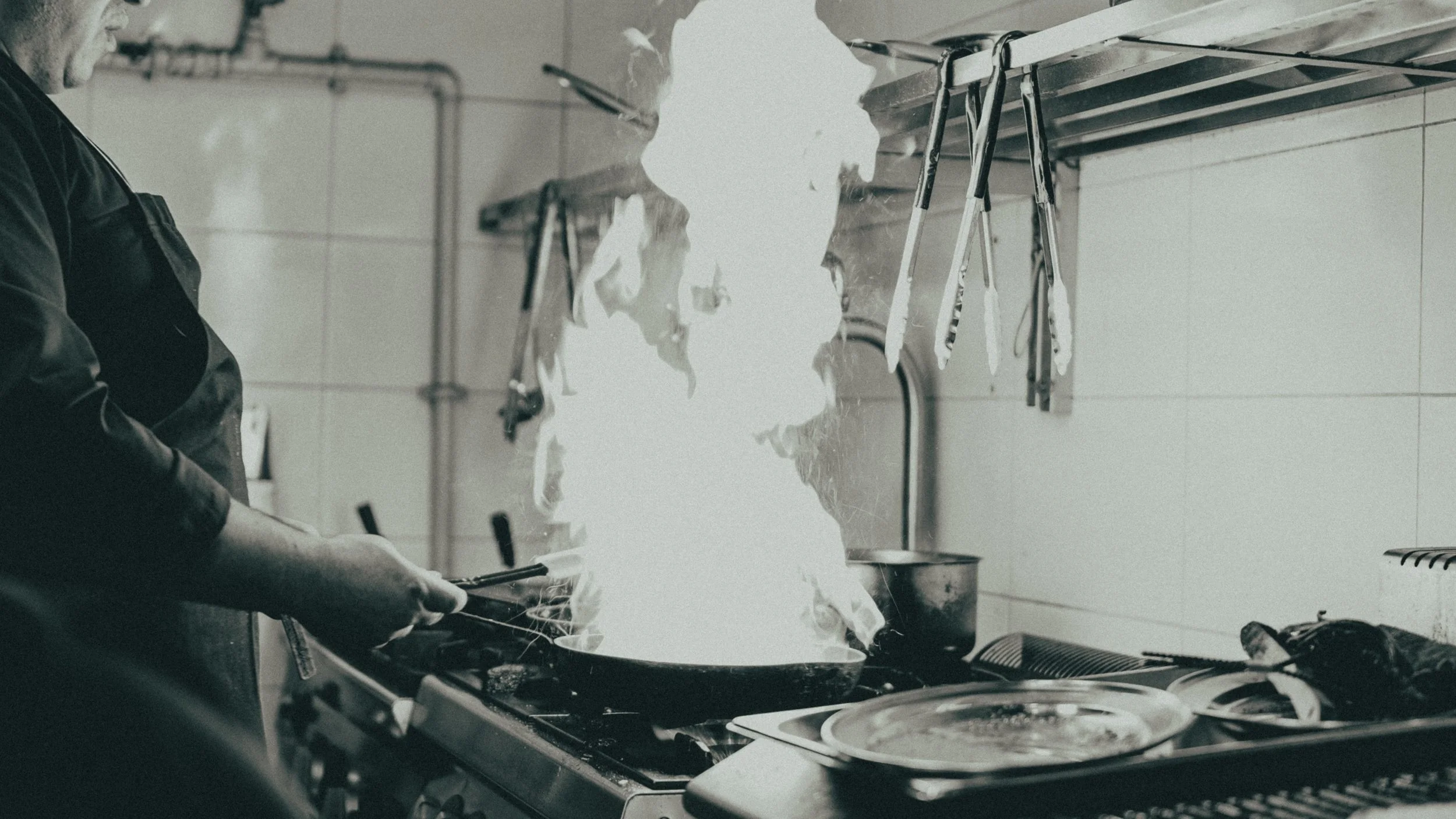 A person cooking on a stove with flames rising as they cook food in a kitchen.