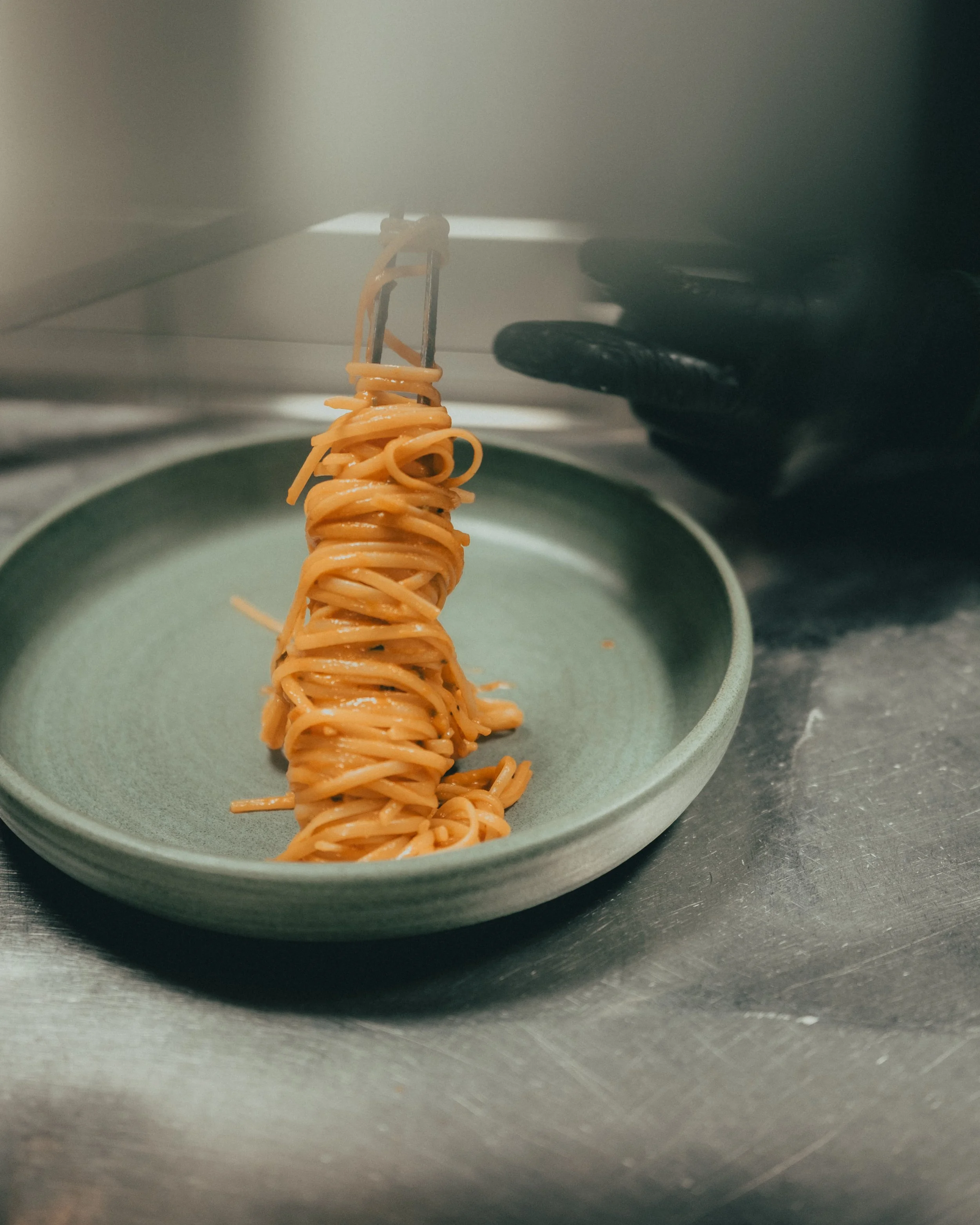 Spaghetti noodles held on a fork, hovering above a pale green bowl on a gray kitchen countertop.