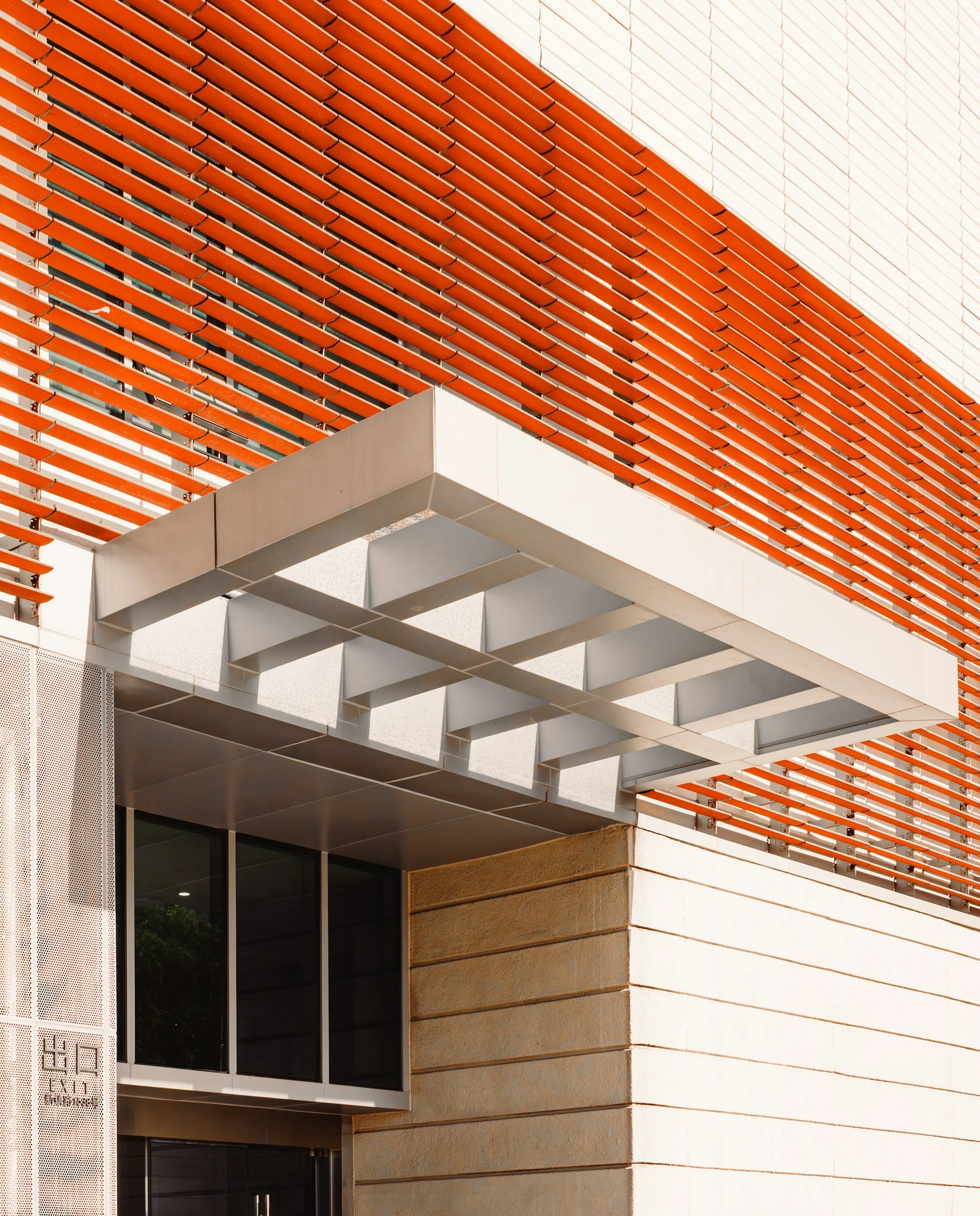 Close-up of modern building facade with orange horizontal slats, white structural elements, beige stone wall, and glass windows.