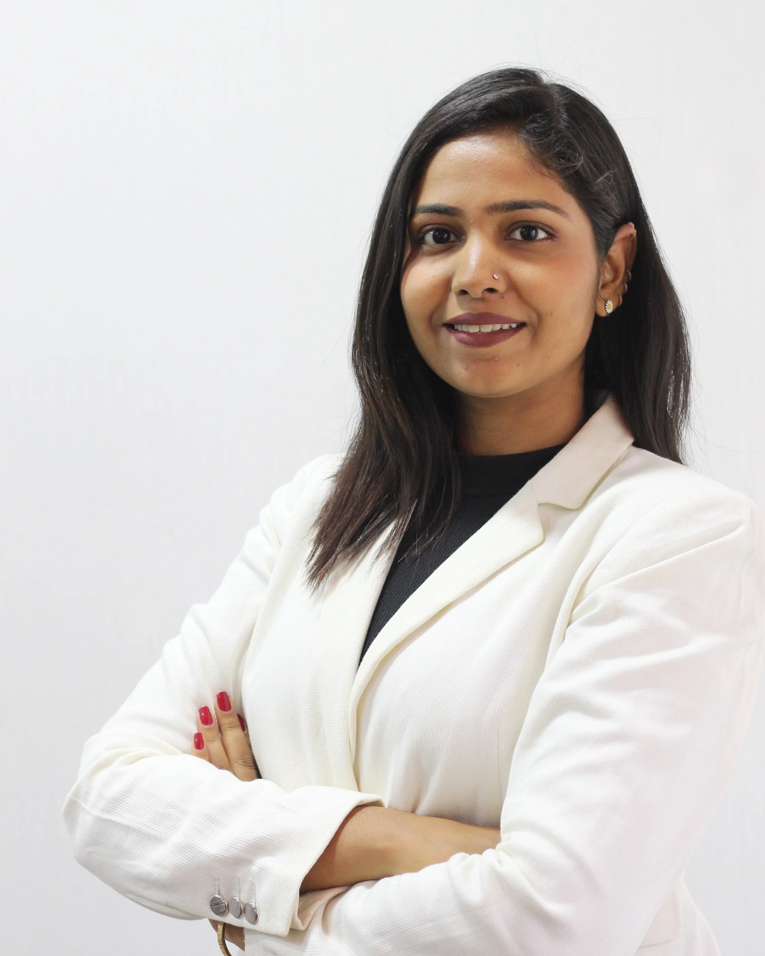 A woman with dark hair, wearing a white blazer and crossed arms, smiling against a plain white background.