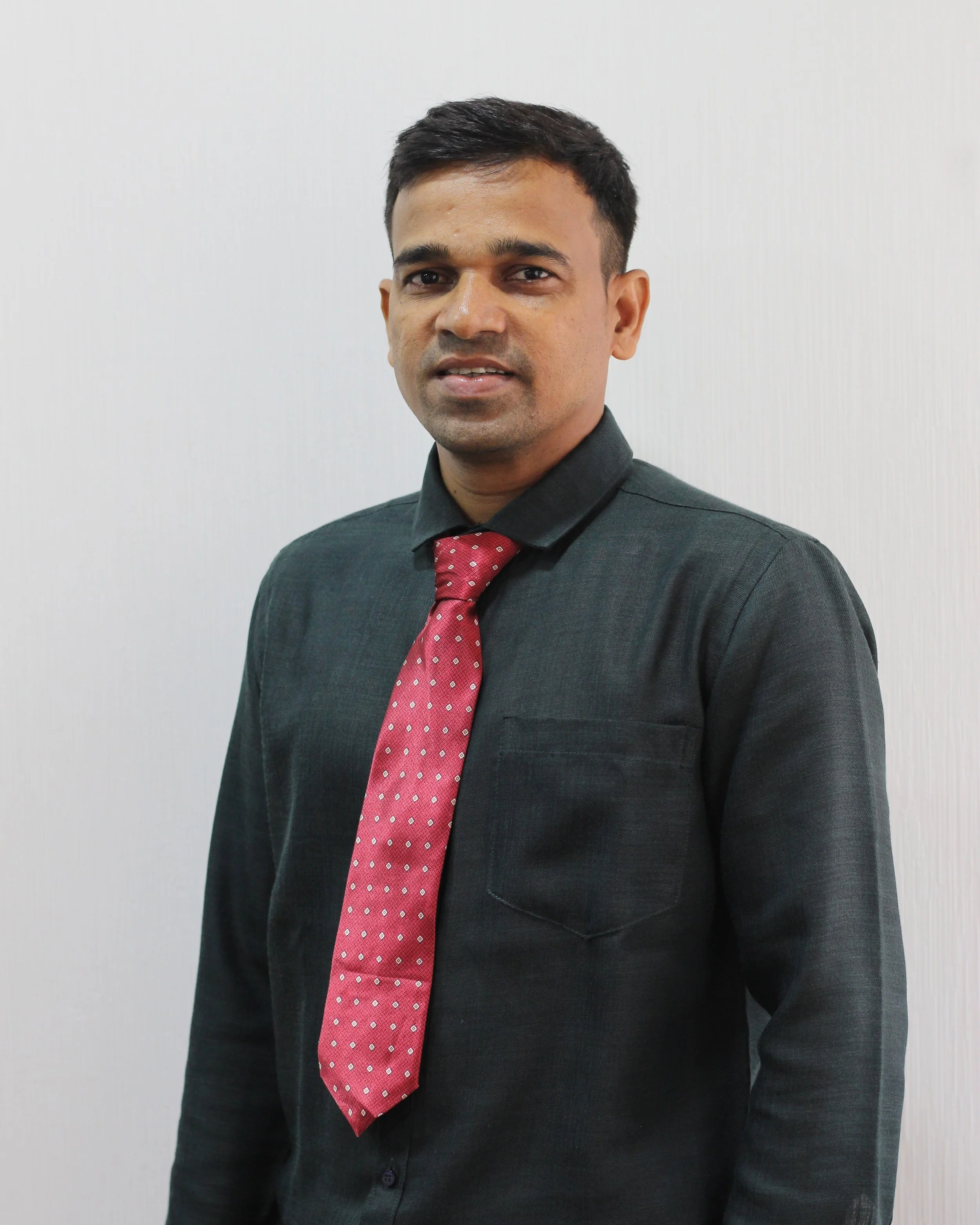 A man wearing a black dress shirt and a red tie with white dots standing against a plain white wall.