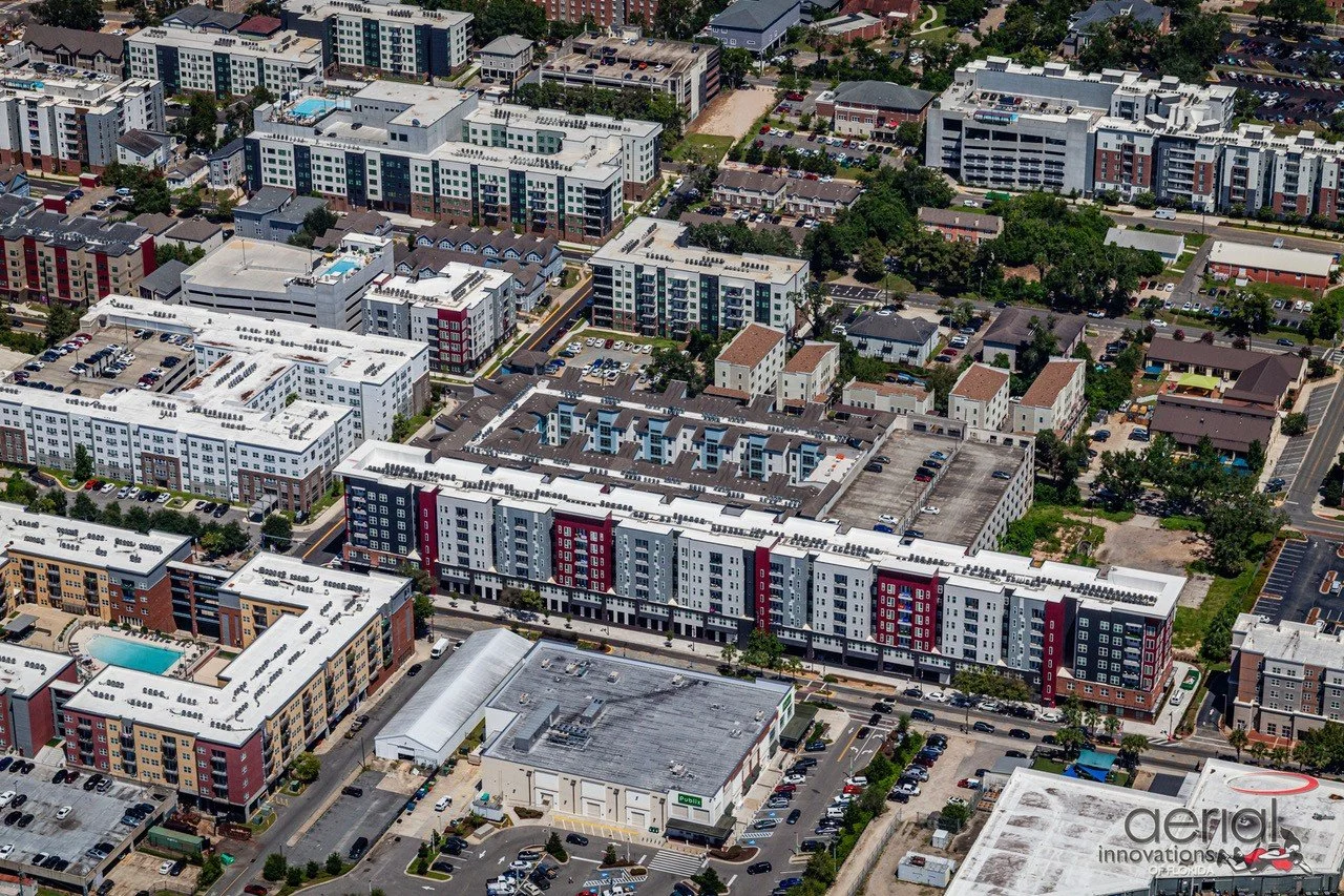 Aerial view of a cityscape with modern apartment buildings, parking lots, and surrounding greenery.