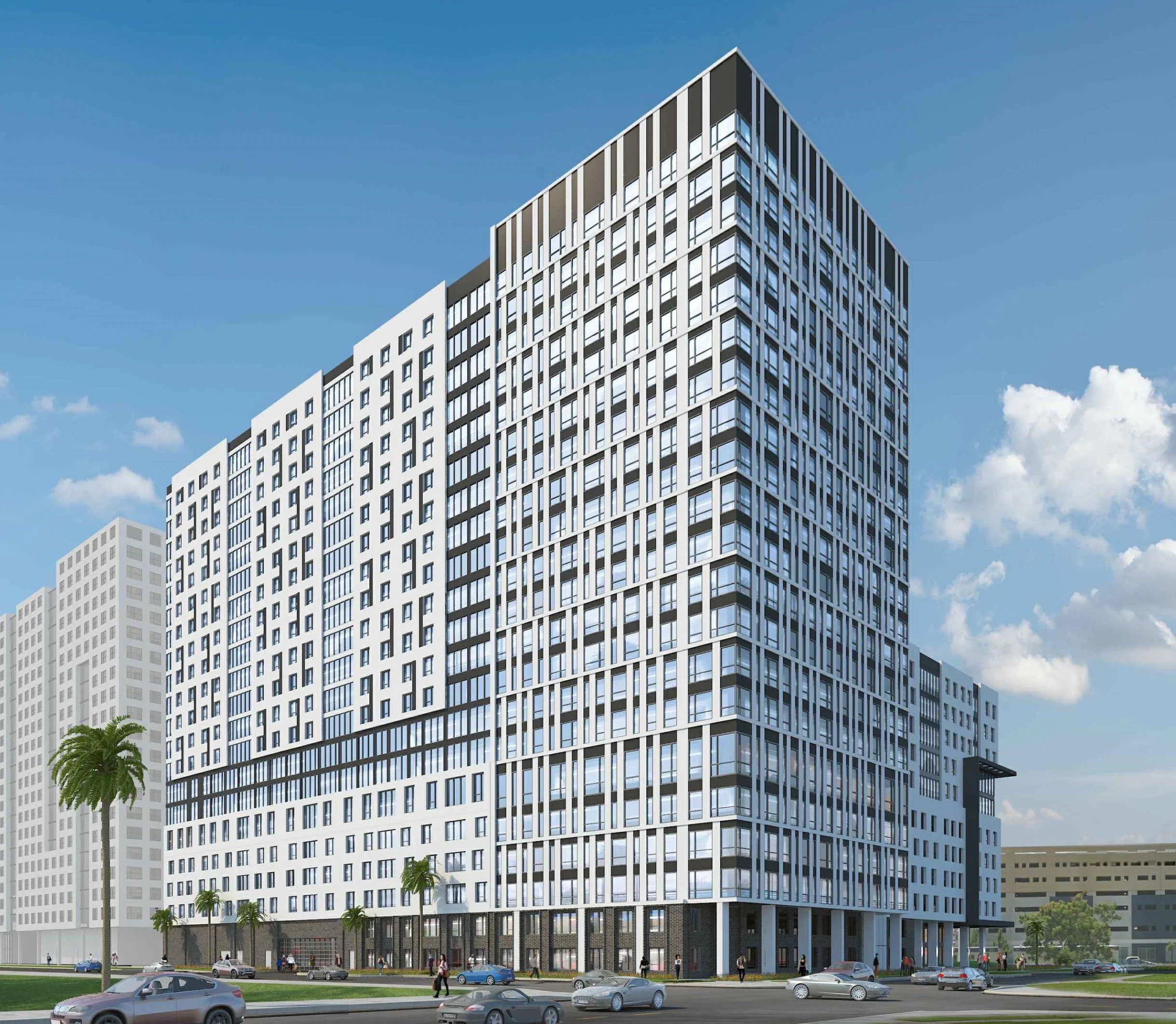 Modern multi-story apartment building with numerous windows, a glass facade, and a geometric design. Palm trees lining the street in front, cars parked along the road, and people walking nearby, under a blue sky with scattered clouds.