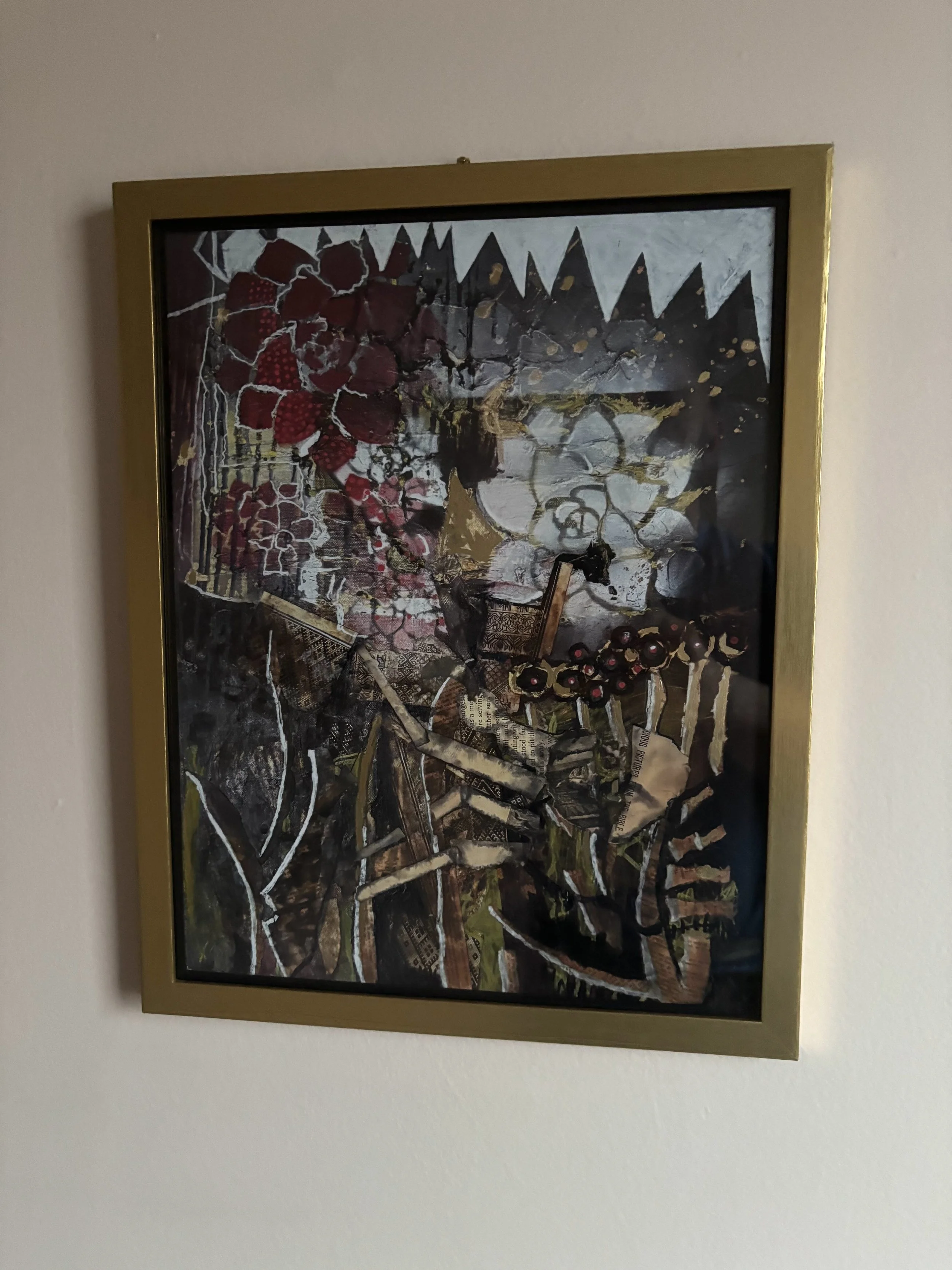 A framed abstract painting with a combination of earthy and dark colors, featuring floral and geometric patterns on a wall.