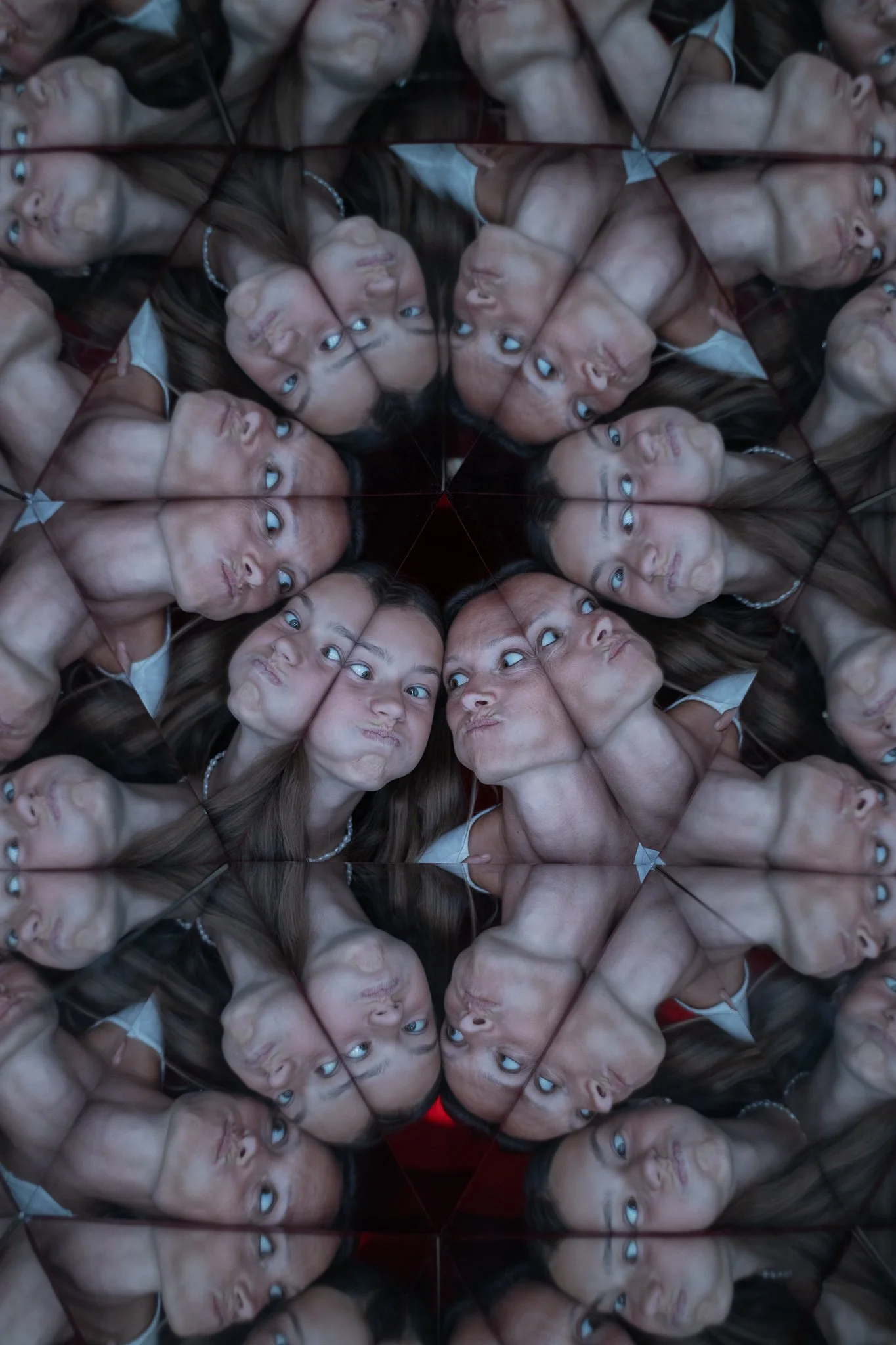 Multiple reflections of a young woman with long dark hair and a pearl necklace, making various facial expressions, seen through a multifaceted mirror, creating an optical illusion of many faces.