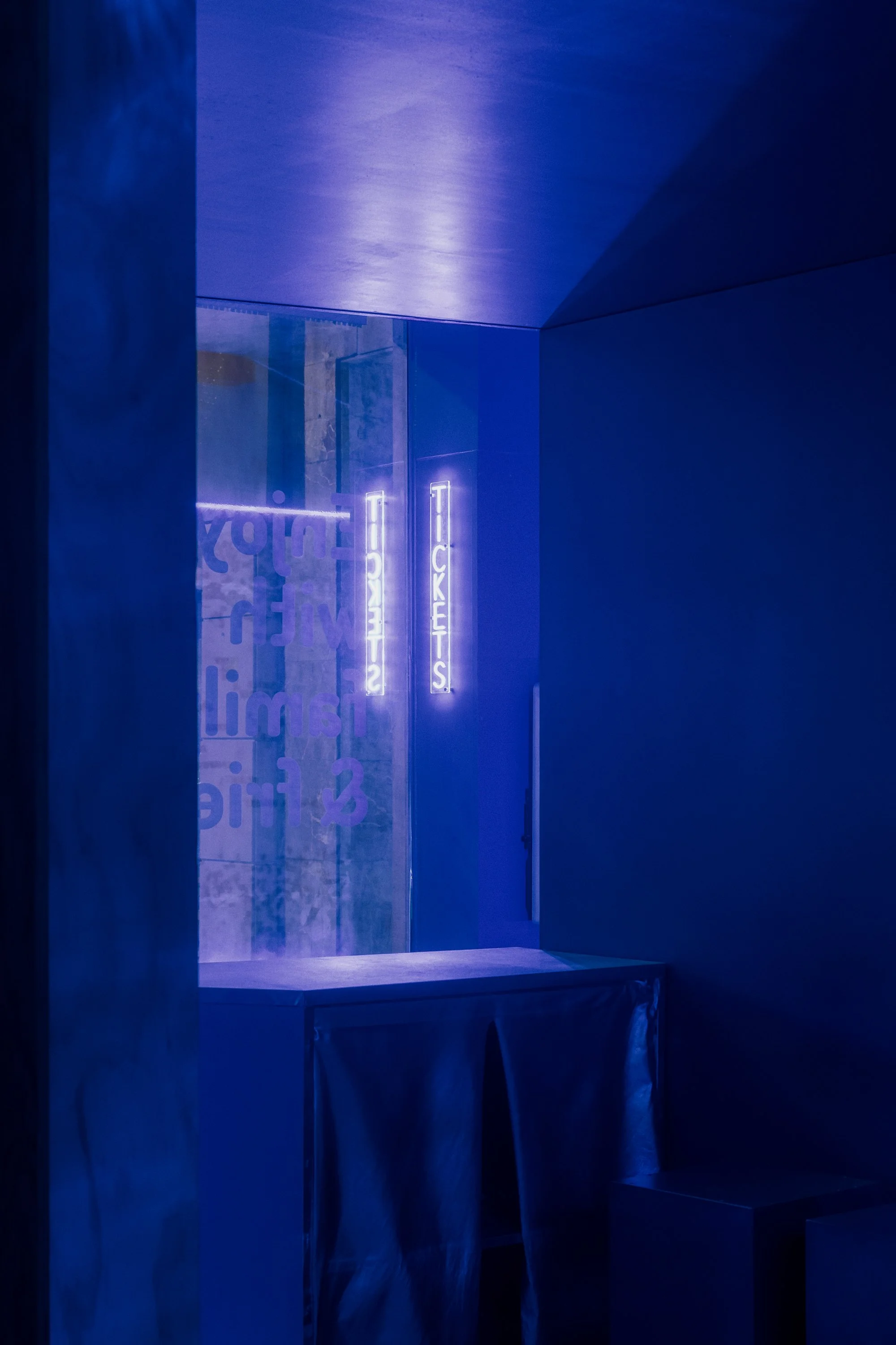Blue neon sign that reads 'TICKETS' on a dark wall, with reflections and blurred texts.