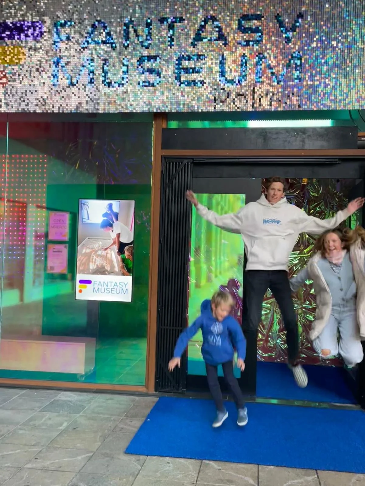 People jumping in front of the entrance to the Fantasy Museum with a colorful holographic sign above the door.